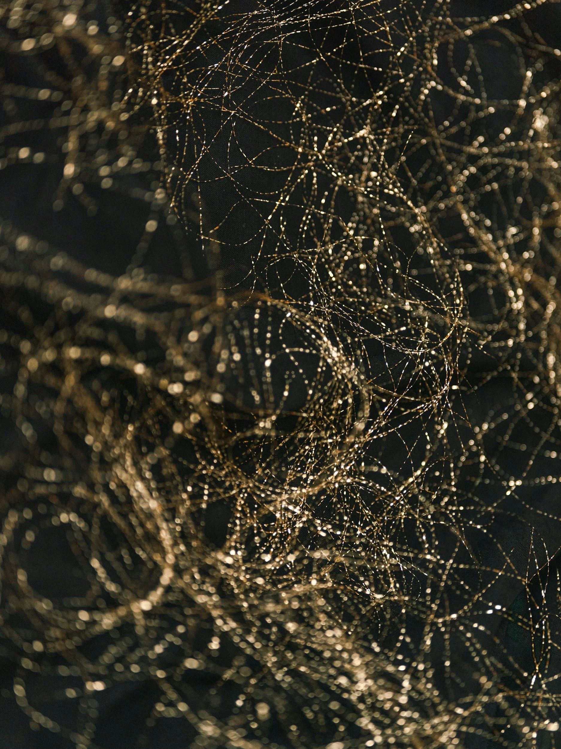 Close-up of a tangled, shimmering gold network of thin, shiny threads or wires against a dark background.