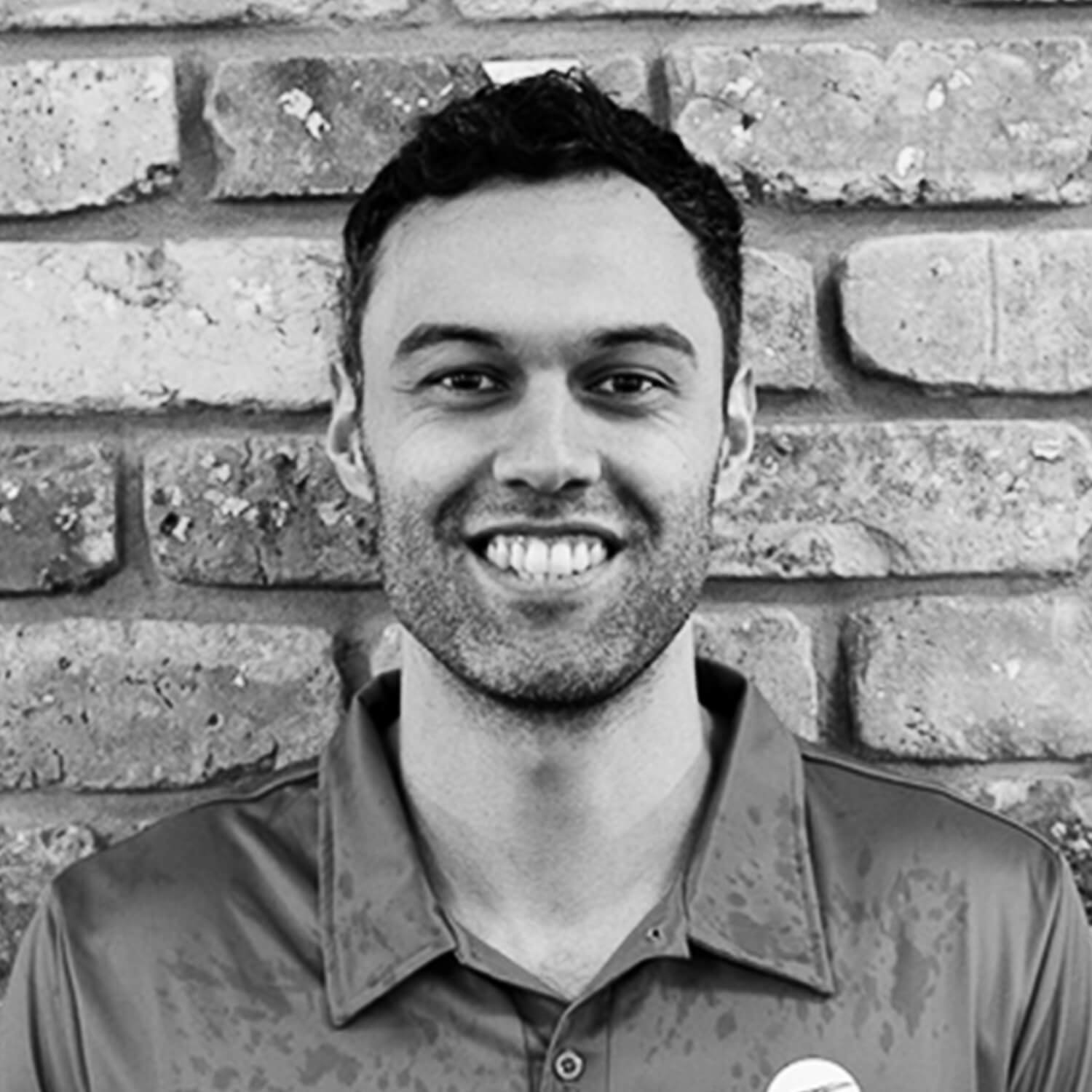 Picture of Josh. He is smiling and outdoors. There is a brick wall behind him.