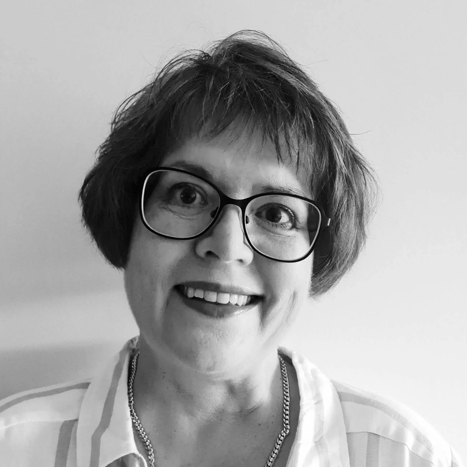 Picture of Jane, she is smiling. She has short hair and wears glasses. 