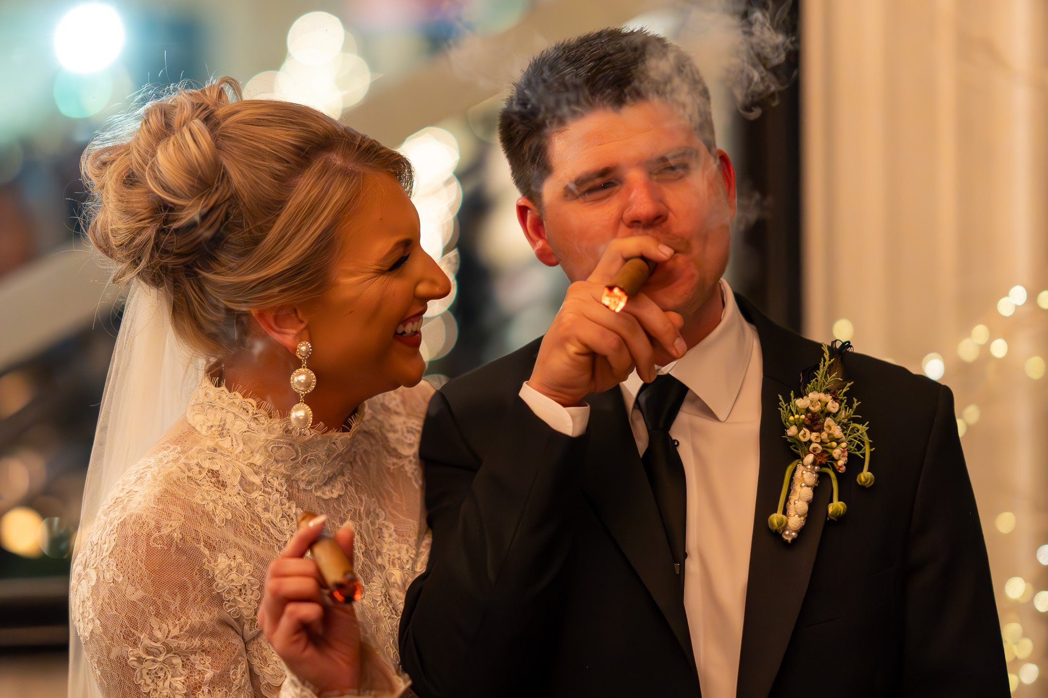 Bride and groom celebrating with cigars, bride smiling, groom smoking.