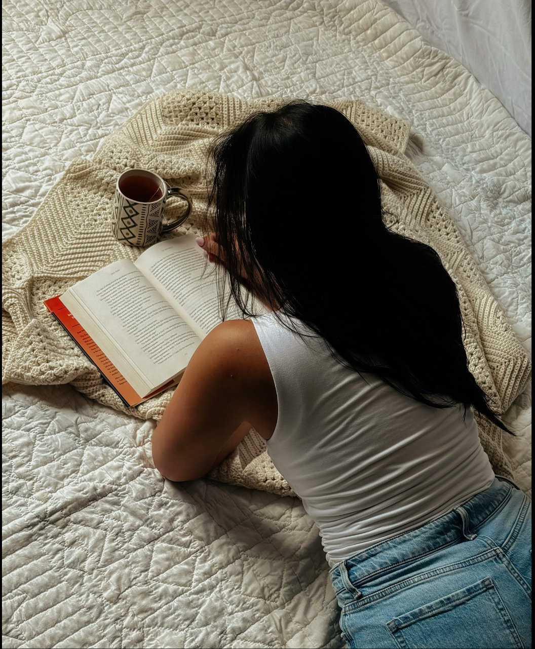 Woman lying on a bed drinking a beverage and reading through notes.