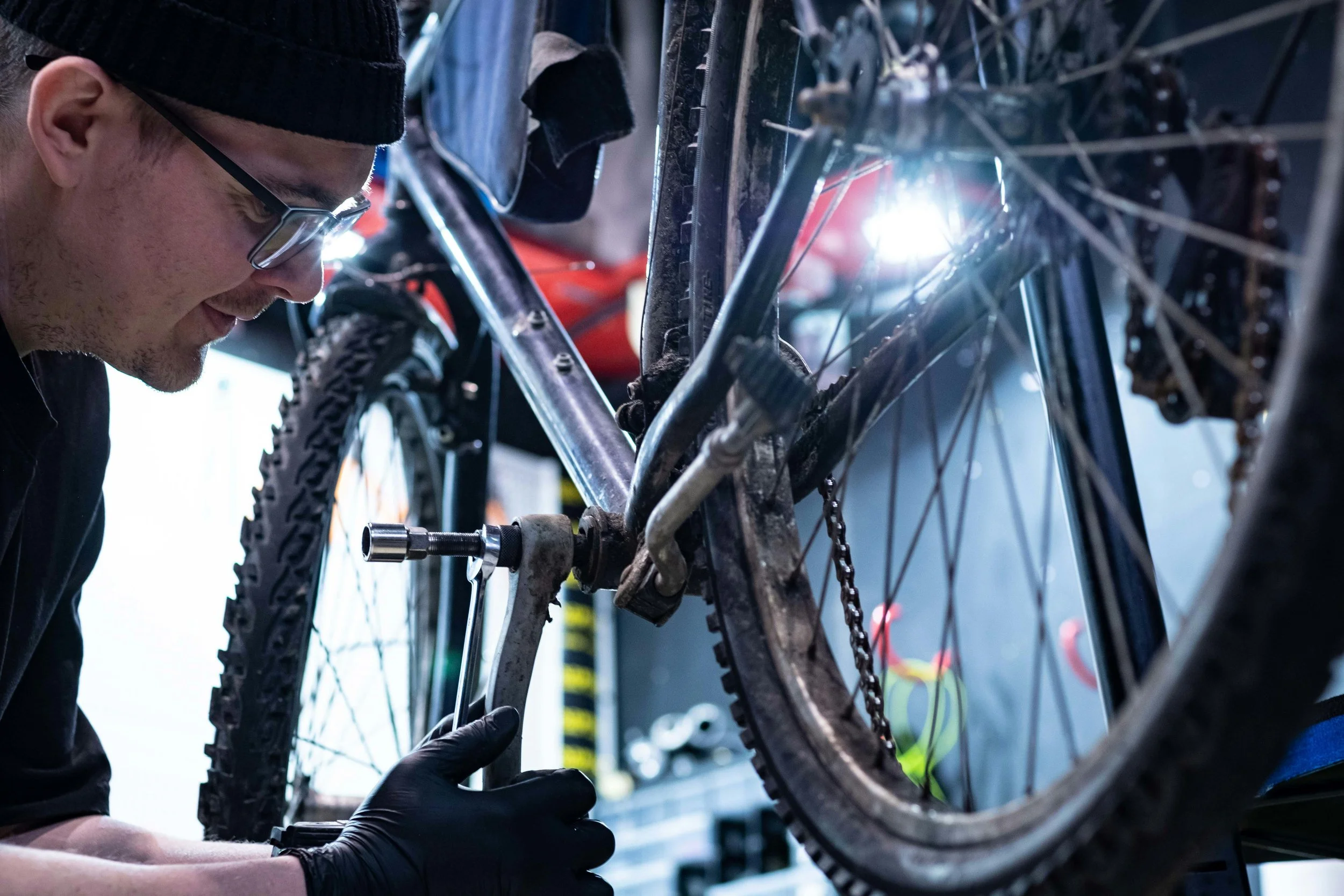A person wearing glasses and black gloves working on a bicycle in a repair shop.