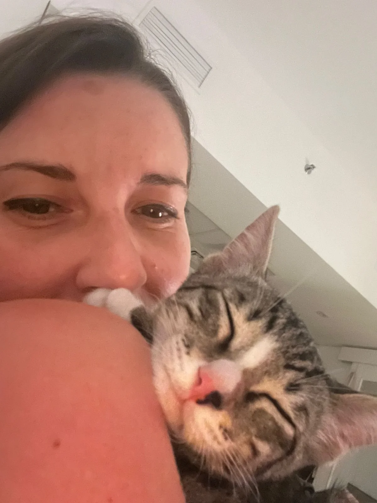 A woman hugging a sleeping tabby cat with closed eyes