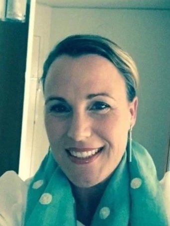 Smiling woman with short hair wearing a teal scarf and sitting indoors.