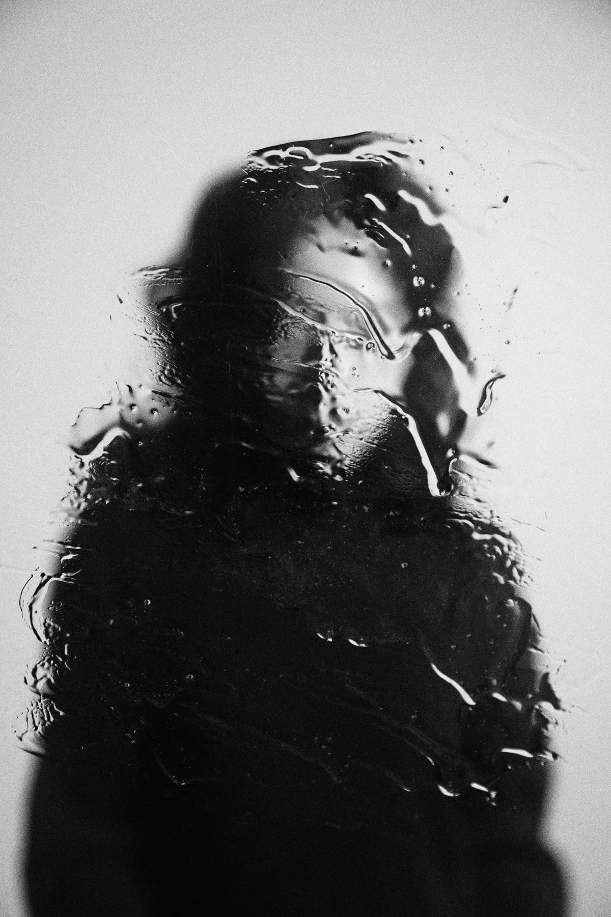 Black and white abstract image of a person's silhouette behind a textured glass surface with water or liquid.