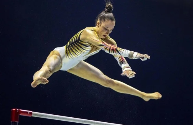 Gymnast performing a split leap on uneven bars in a competition.