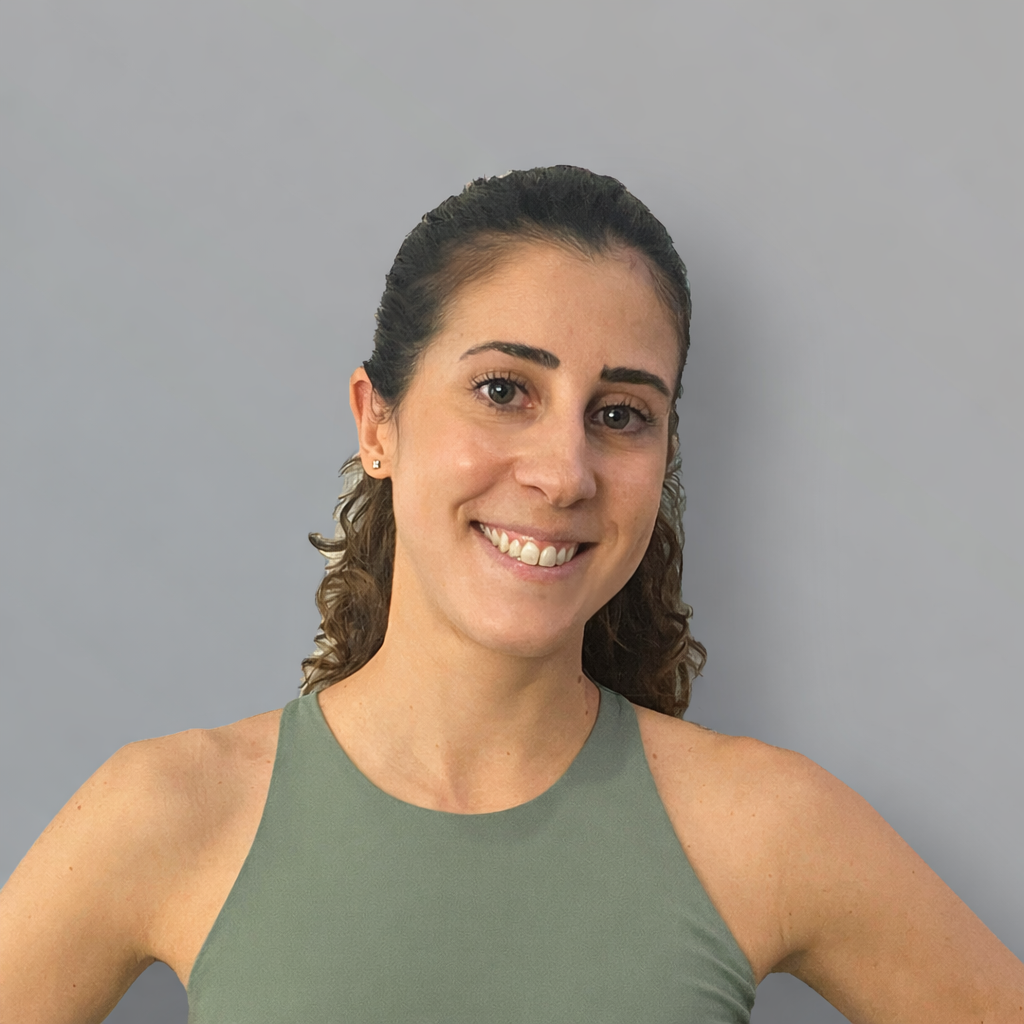Mujer joven con cabello rizado atado, sonriendo, con camiseta sin mangas de color verde y humedad en el cabello, frente a un fondo gris.