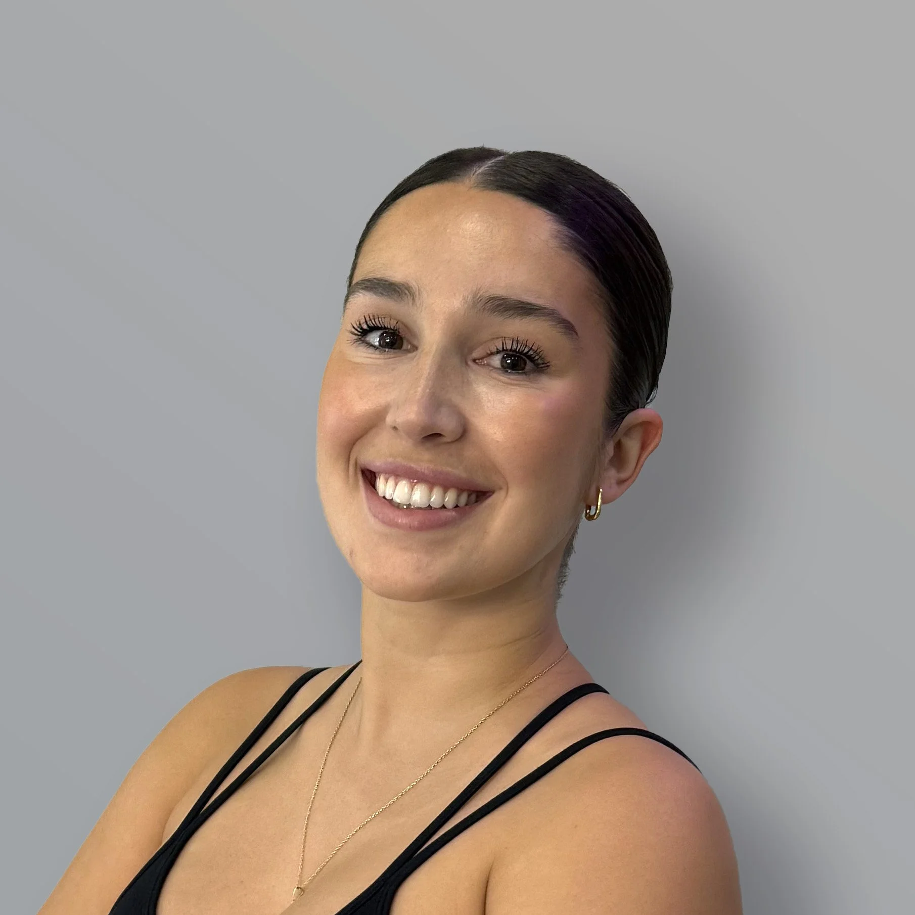 Jovencita sonriendo con cabello oscuro y liso, usando un top sin mangas y pendientes dorados.
