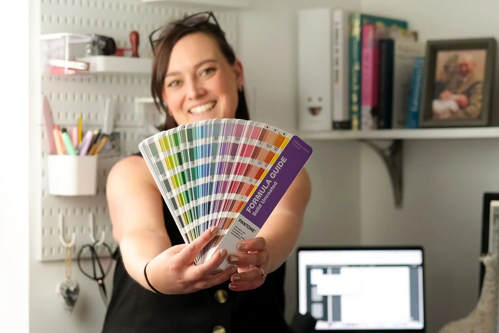 A woman smiling and holding up color swatches in front of her in a home office.