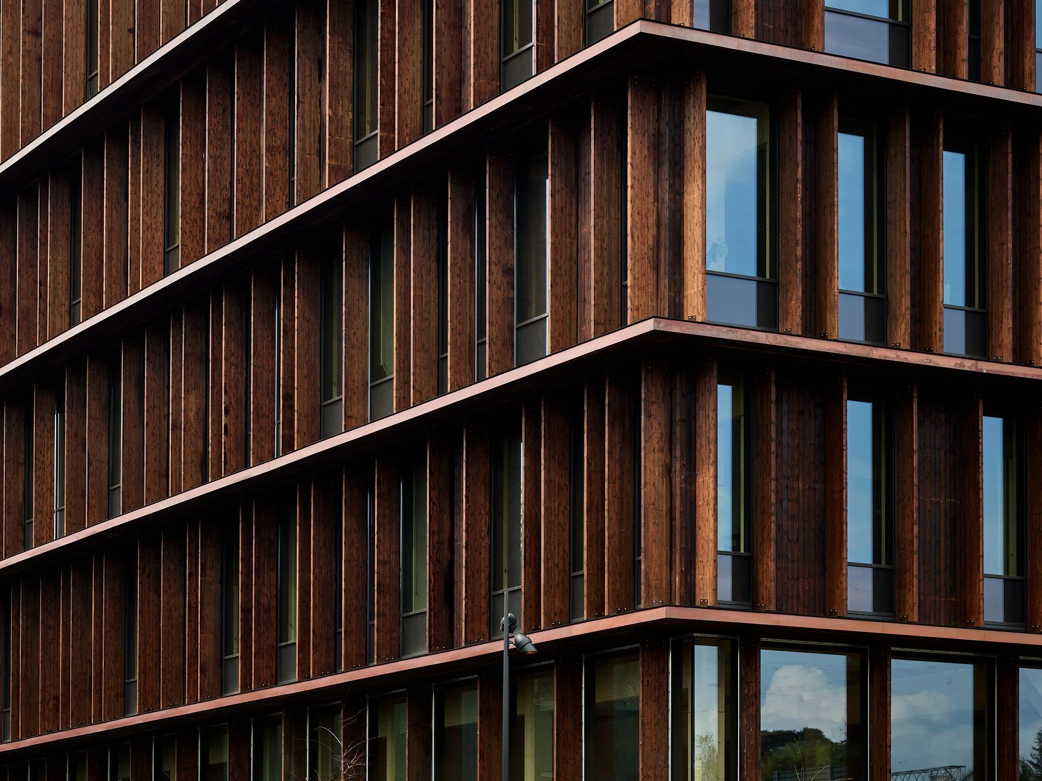 Close-up view of a modern building with a wooden facade, large windows, and horizontal white trim.