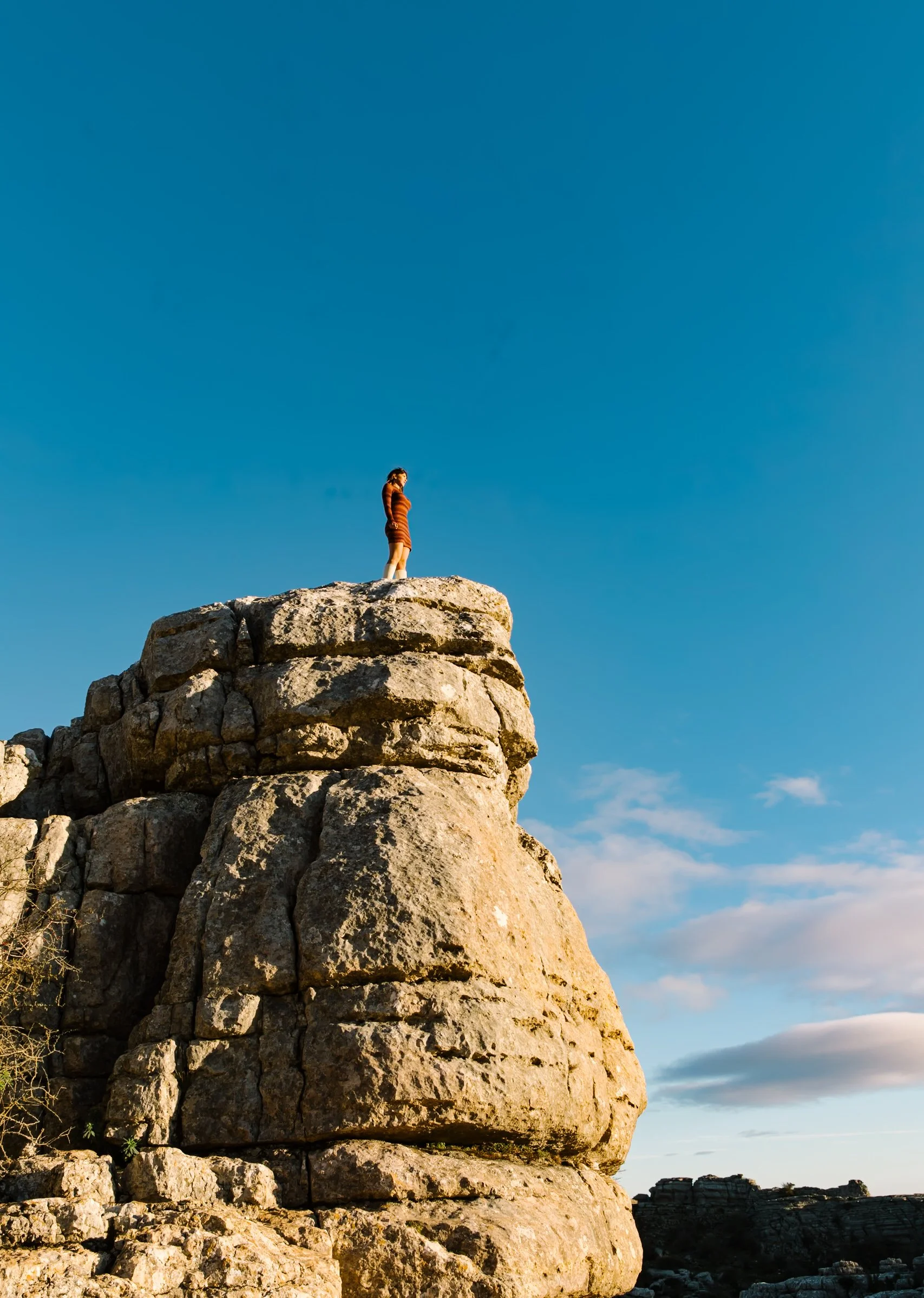 mujer subida en lo alto de una colida de piedra macica con el fondo azul despejado de fondo en las carcavas