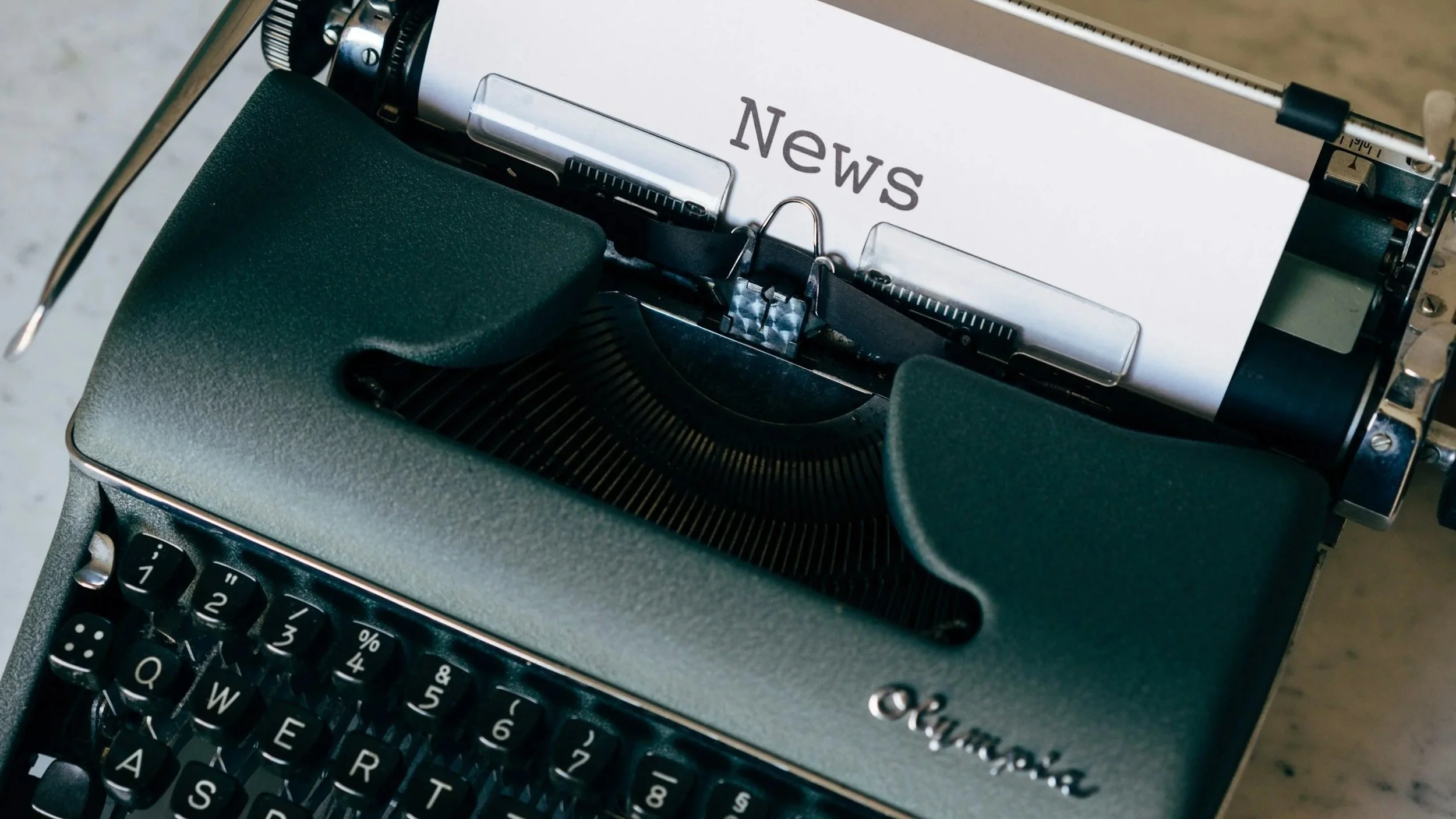 Close-up of a vintage typewriter with a sheet of paper labeled 'News' inserted, showing keys and parts of the typewriter