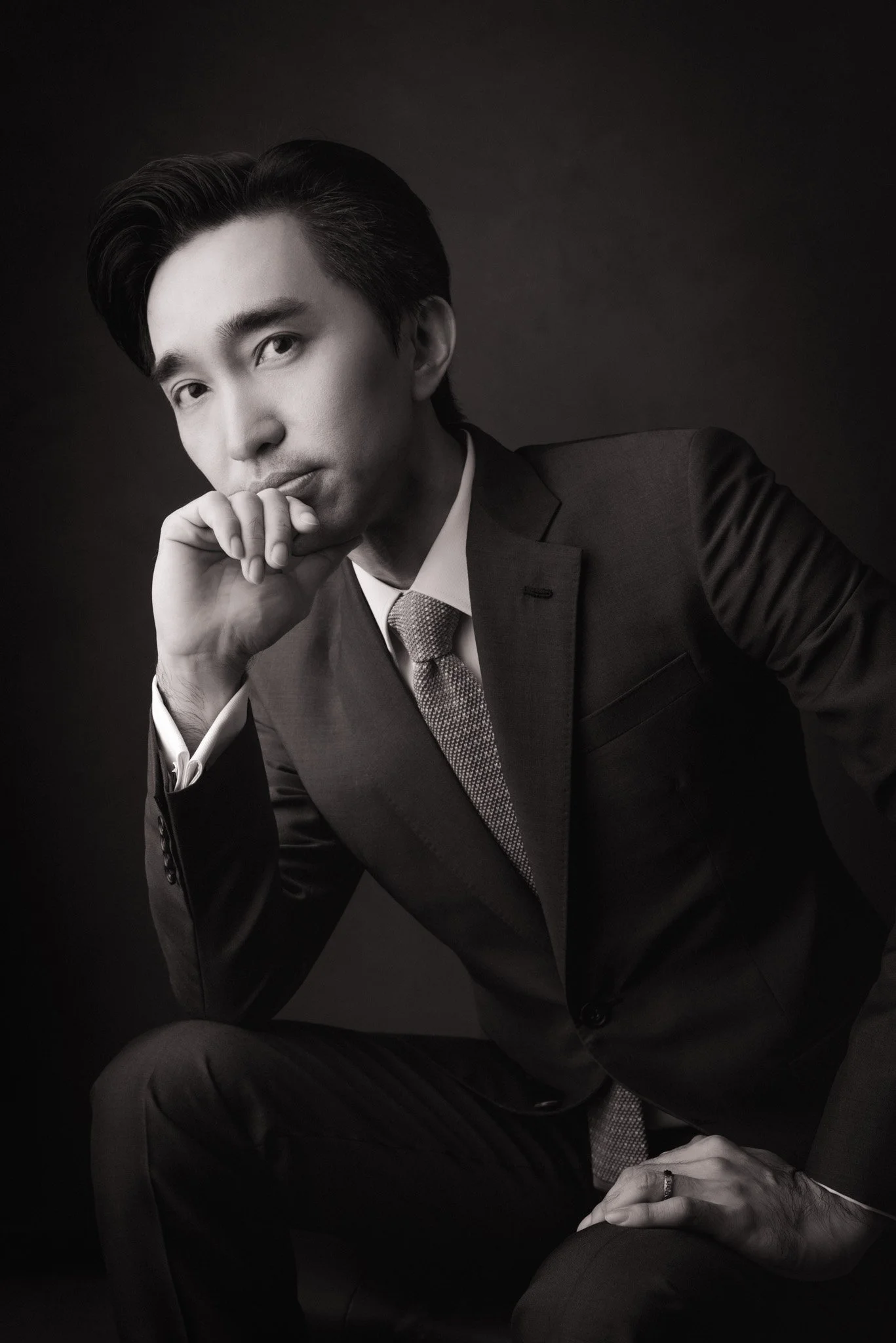 Black and white portrait of a man in a suit, with his hand resting on his chin, looking thoughtfully at the camera.