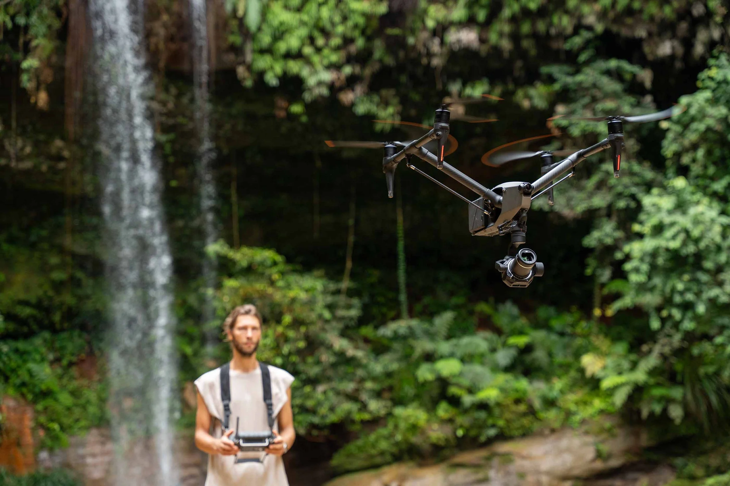 Ein Mann mit einem Drone im Wald near einem Wasserfall im Hintergrund.