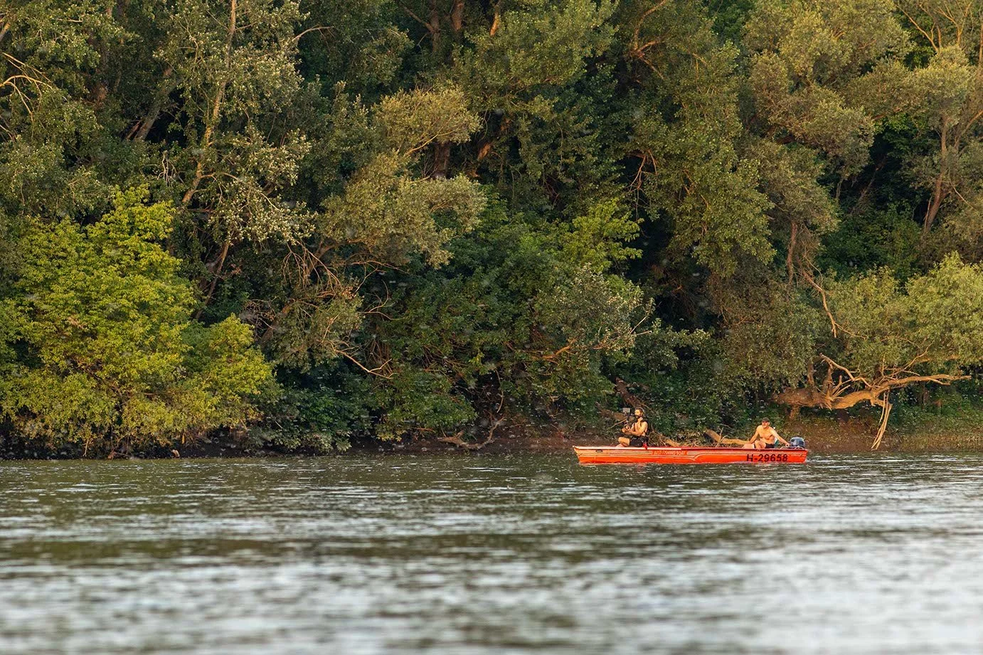 Zwei Personen in einem roten Boot auf einem Fluss, umgeben von dichten grünen Bäumen.