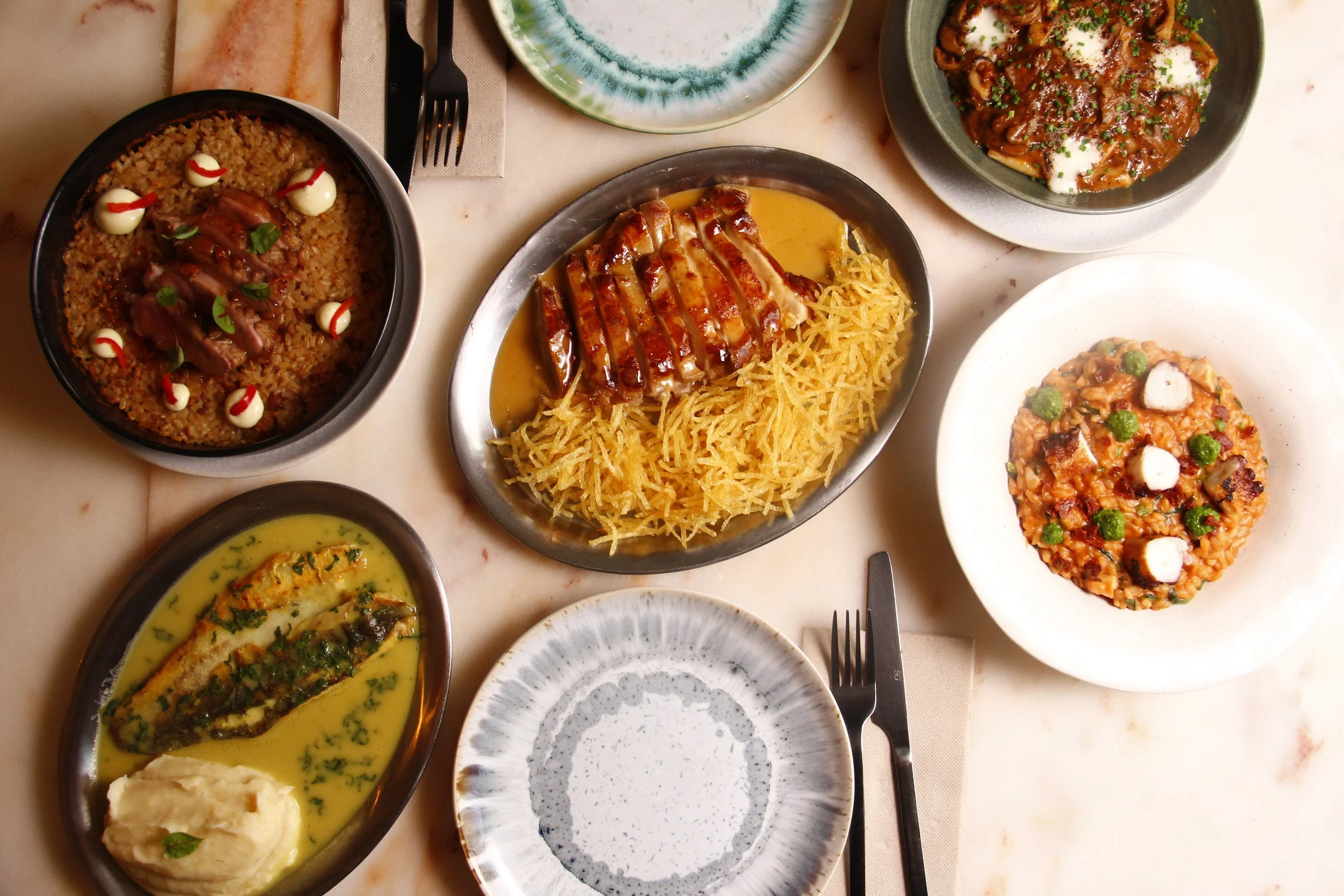 Pratos de cozinha mediterrânica do restaurante Cobaia em Alvalade, Lisboa — frango, robalo e arroz, entre outros, servidos numa mesa posta.