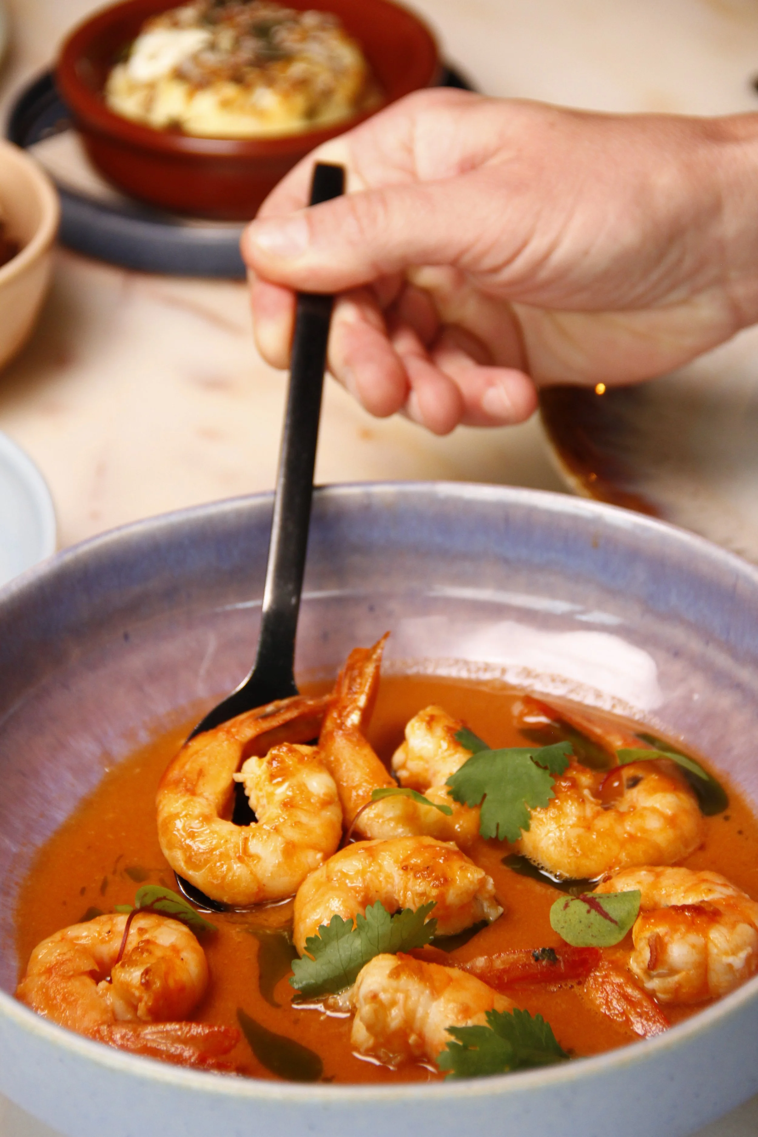 Close-up de pessoa a provar o Camarão Salteado com molho bisque do Restaurante Cobaia em Alvalade, Lisboa numa tigela de cerâmica.