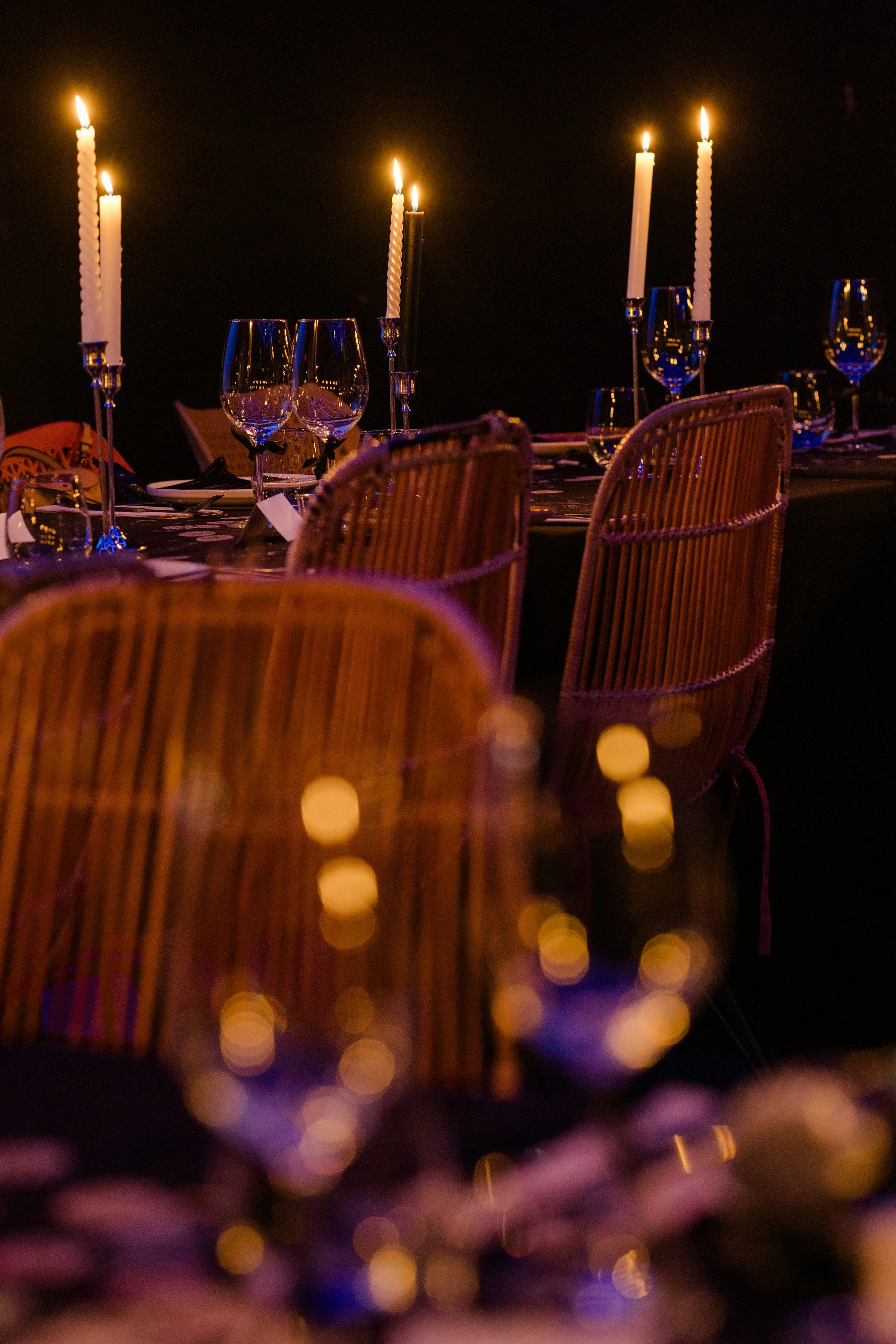 Mesa decorada com copos de vinho e taças, com velas acesas em castiçais altos, em ambiente de jantar elegante e aconchegante no espaço Poolside em Alvalade.