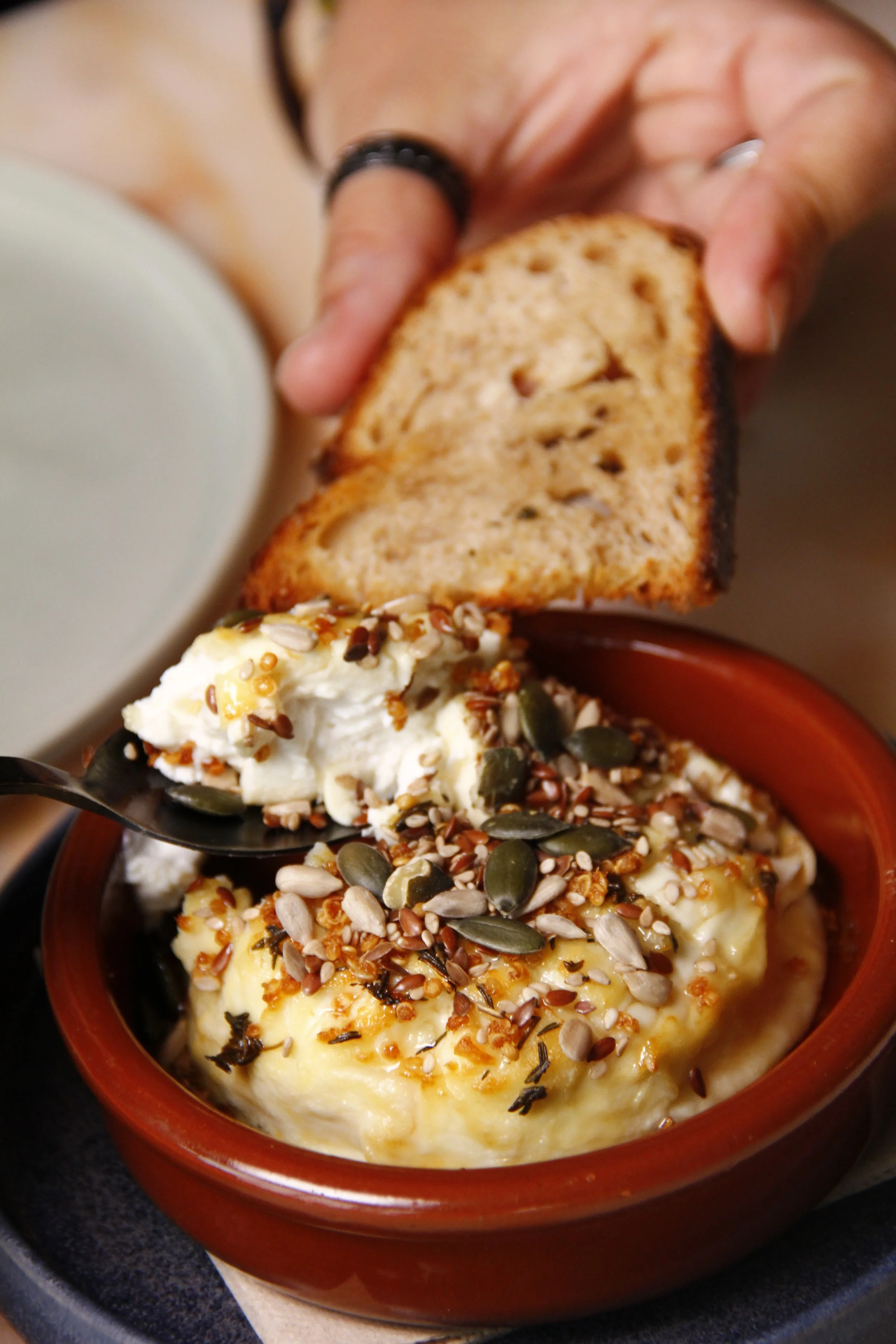 Close-up de pessoa a colocar queijo cremoso com sementes variadas em cima de pão torrado no Restaurante Cobaia em Alvalade, Lisboa.