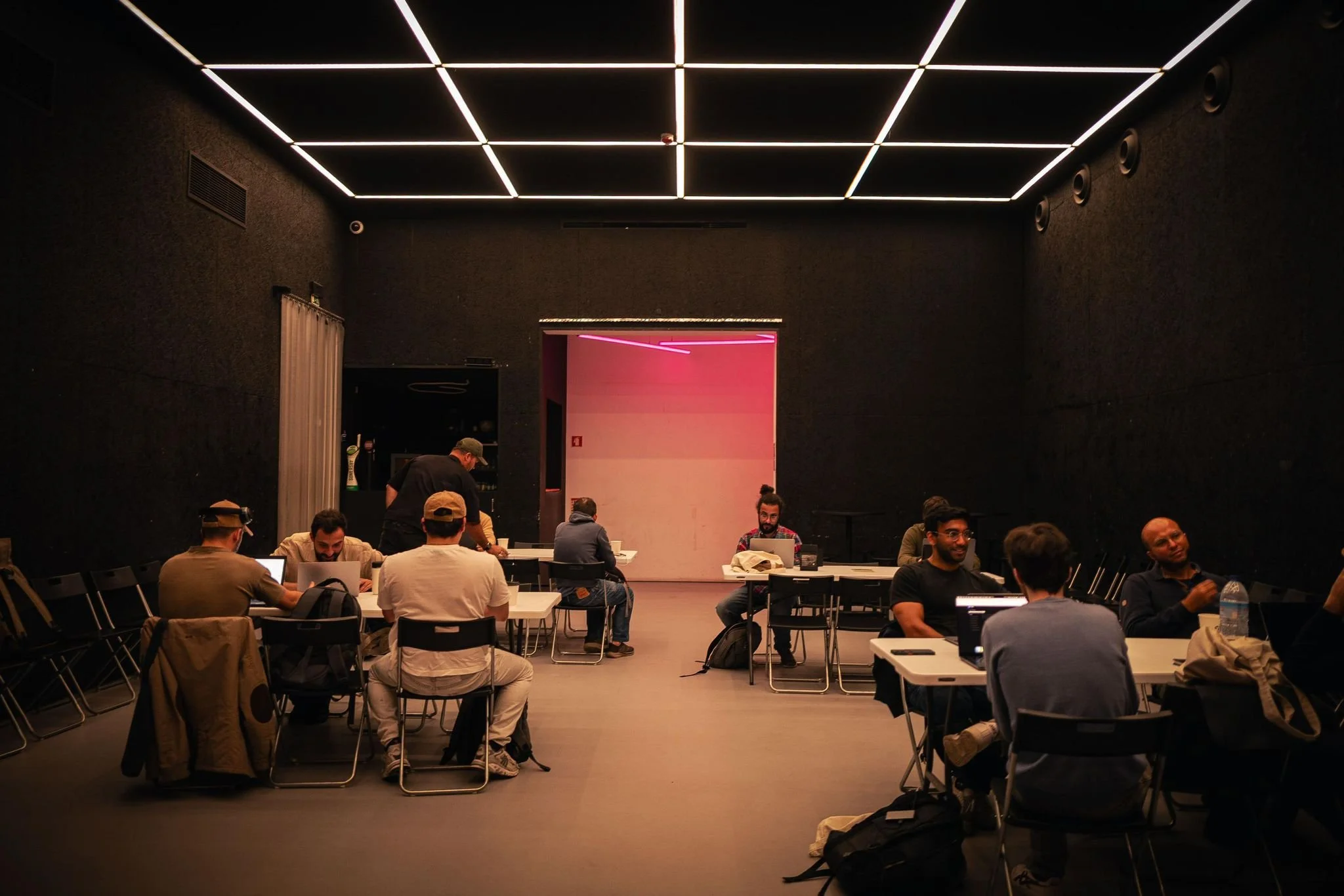 Hackathon no espaço de eventos Poolside em Alvalade, Lisboa, com participantes a trabalhar em computadores e a colaborar em grupo
