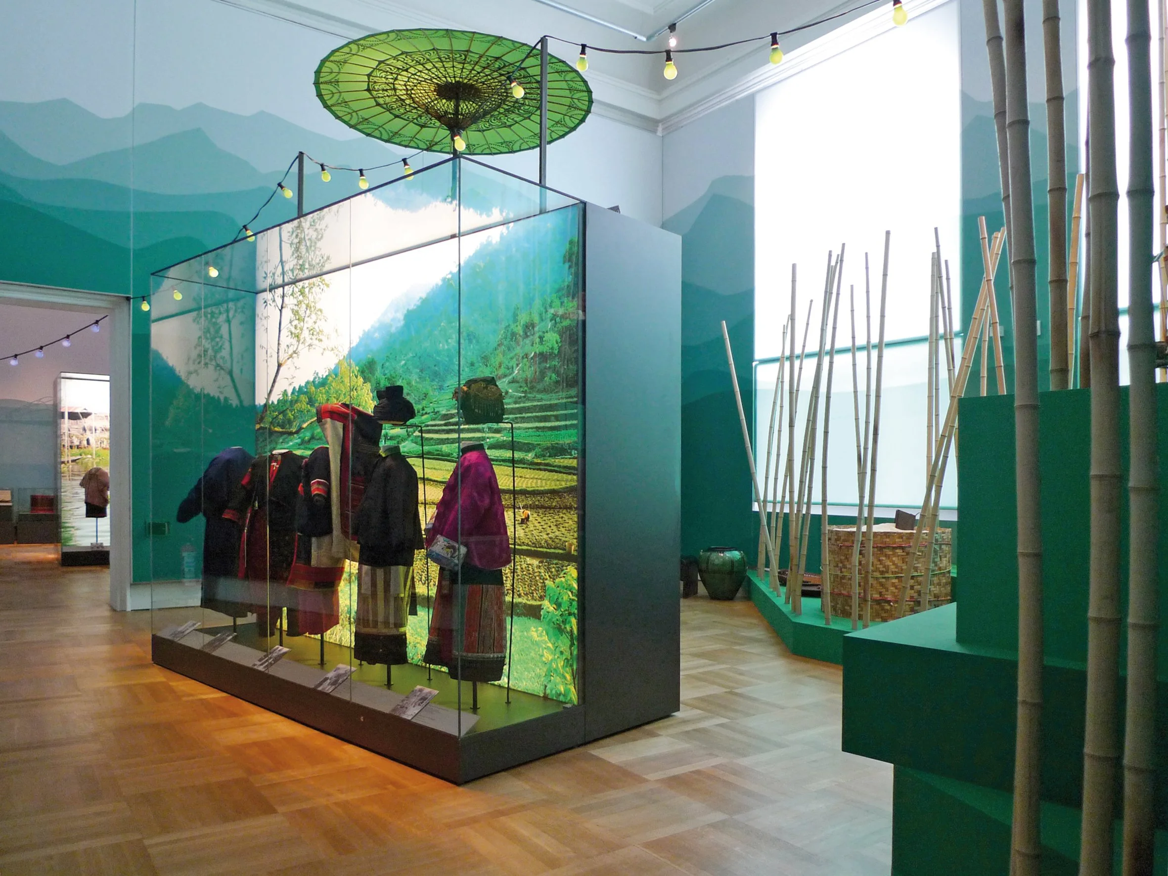 Ausstellung mit traditioneller Kleidung und Landschaftsbild im Hintergrund in einem Museum