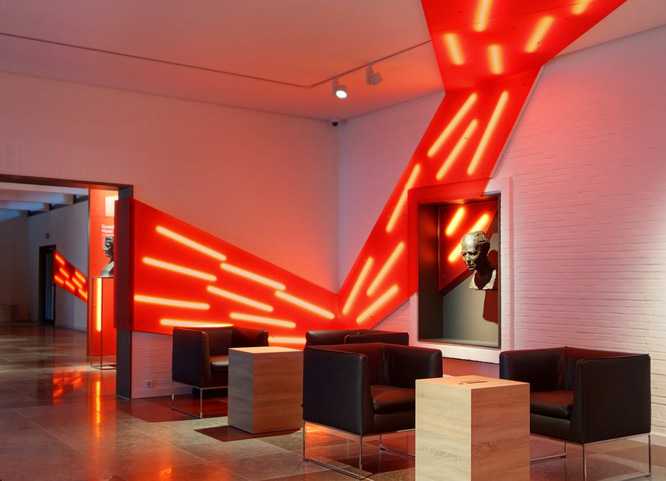 Lounge mit weißen Wänden, schwarzem Ledersitzmöbel und roten Neonlichtern in geometrischer Anordnung