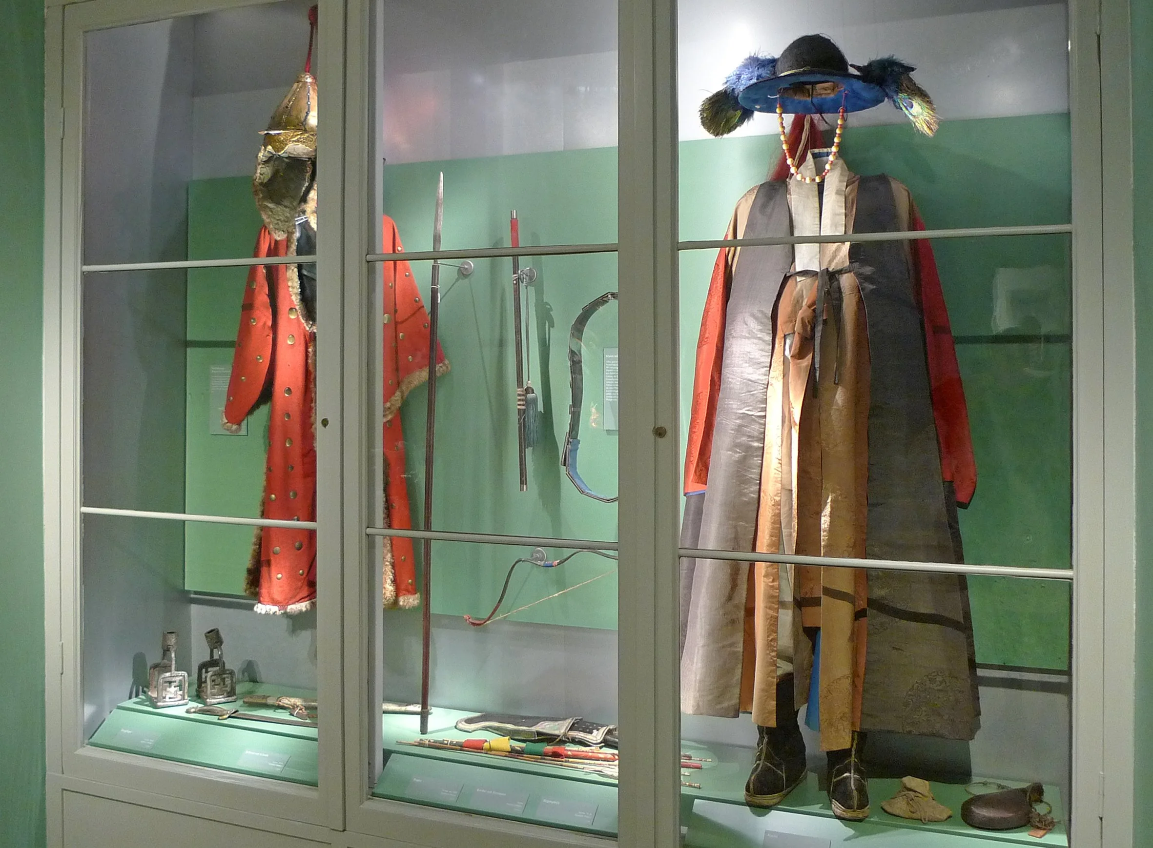 Historische Kleidung und Waffen in einem Schauglas, darunter wiederaufgebaute Kostüme, Rüstungen und Accessoires.