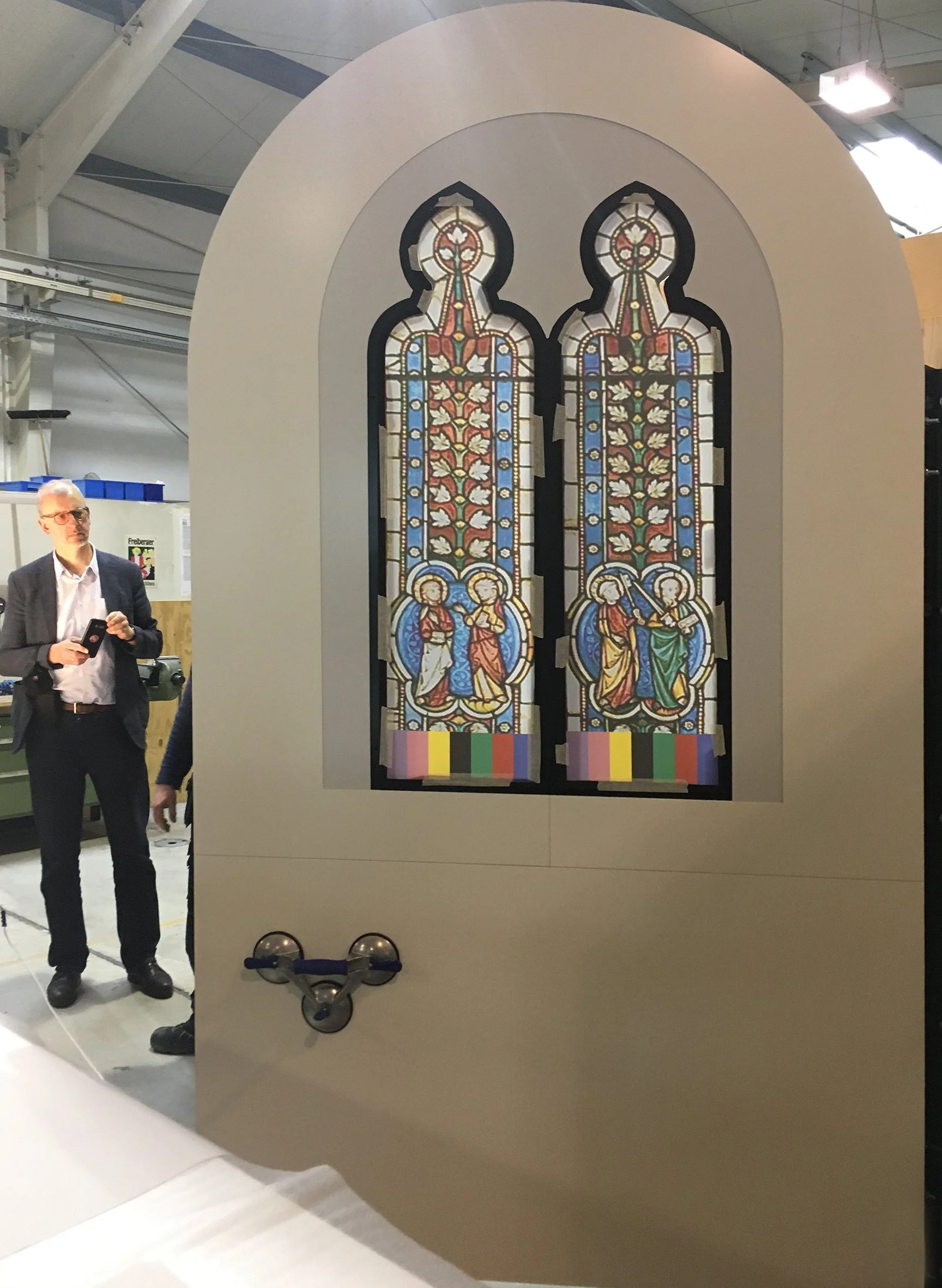 Replika eines bunten Kirchenfensters mit religiösen Szenen, eingefasst in eine Holzrahmen, auf einem Ausstellungstisch