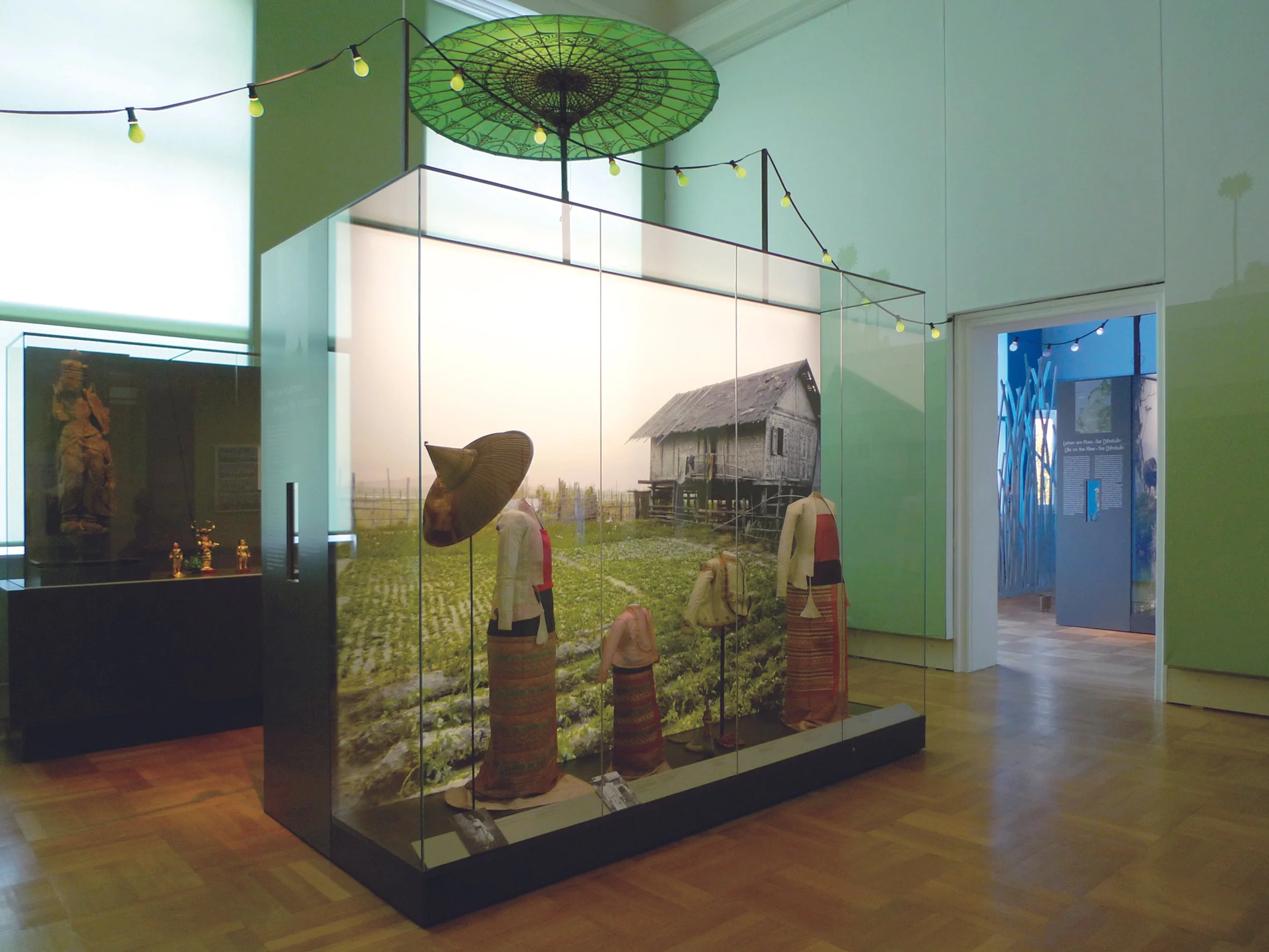 Ausstellung im Museum mit traditioneller Kleidung, Hüten und einer ländlichen Szene im Hintergrund.