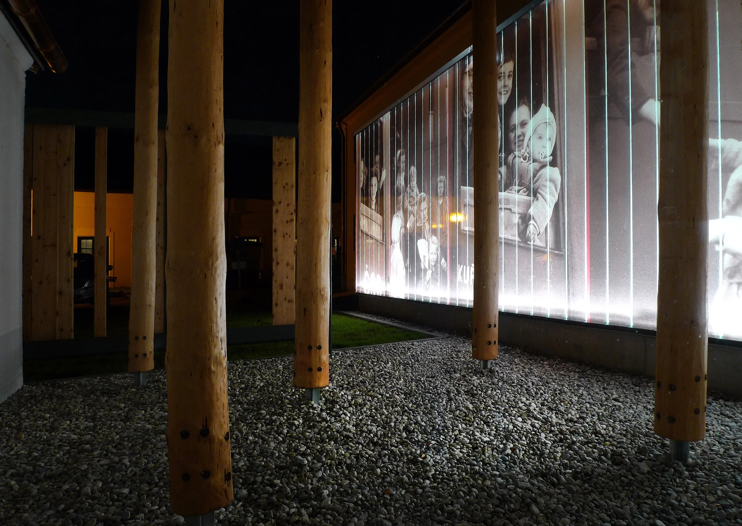 Schwarz-weiße Fotografie von mehreren Personen, im Hintergrund scheinen Kinder auf einer Plattform oder einem Schlitten zu sitzen, auf einer beleuchteten Glasscheibe