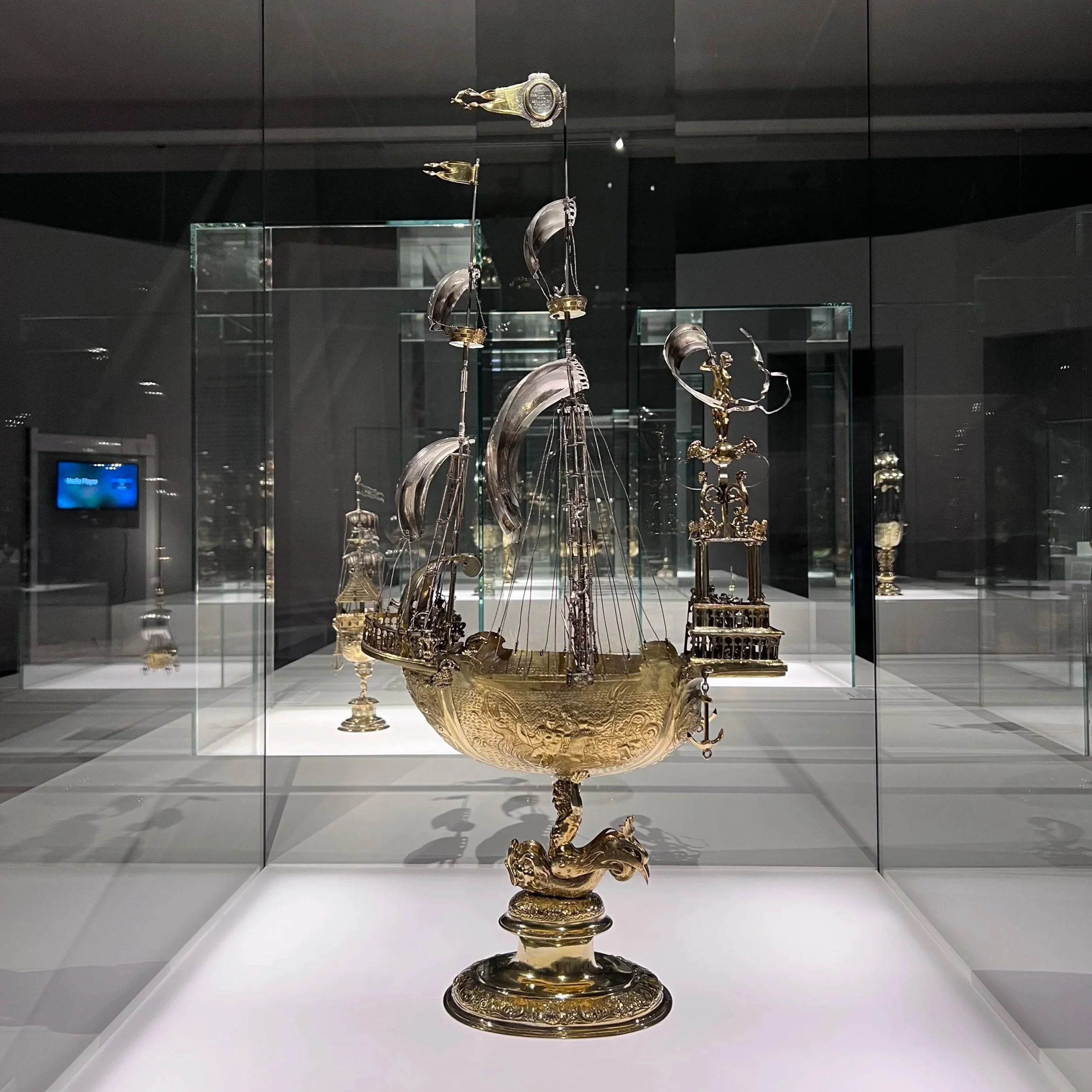 Ein goldener Schiffskelch mit Segelschiffen und Meerwellen, ausgestellt in einem Museum.