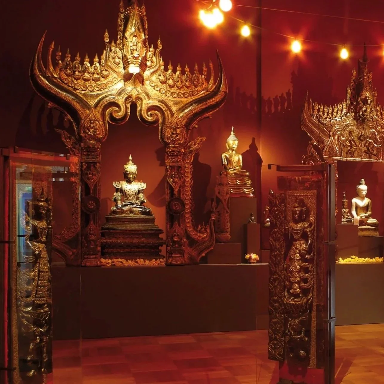 Verschiedene goldene buddhistische Statuen in einem Museum, mit roten Wänden und Bali-ähnlichen Dekorationen.