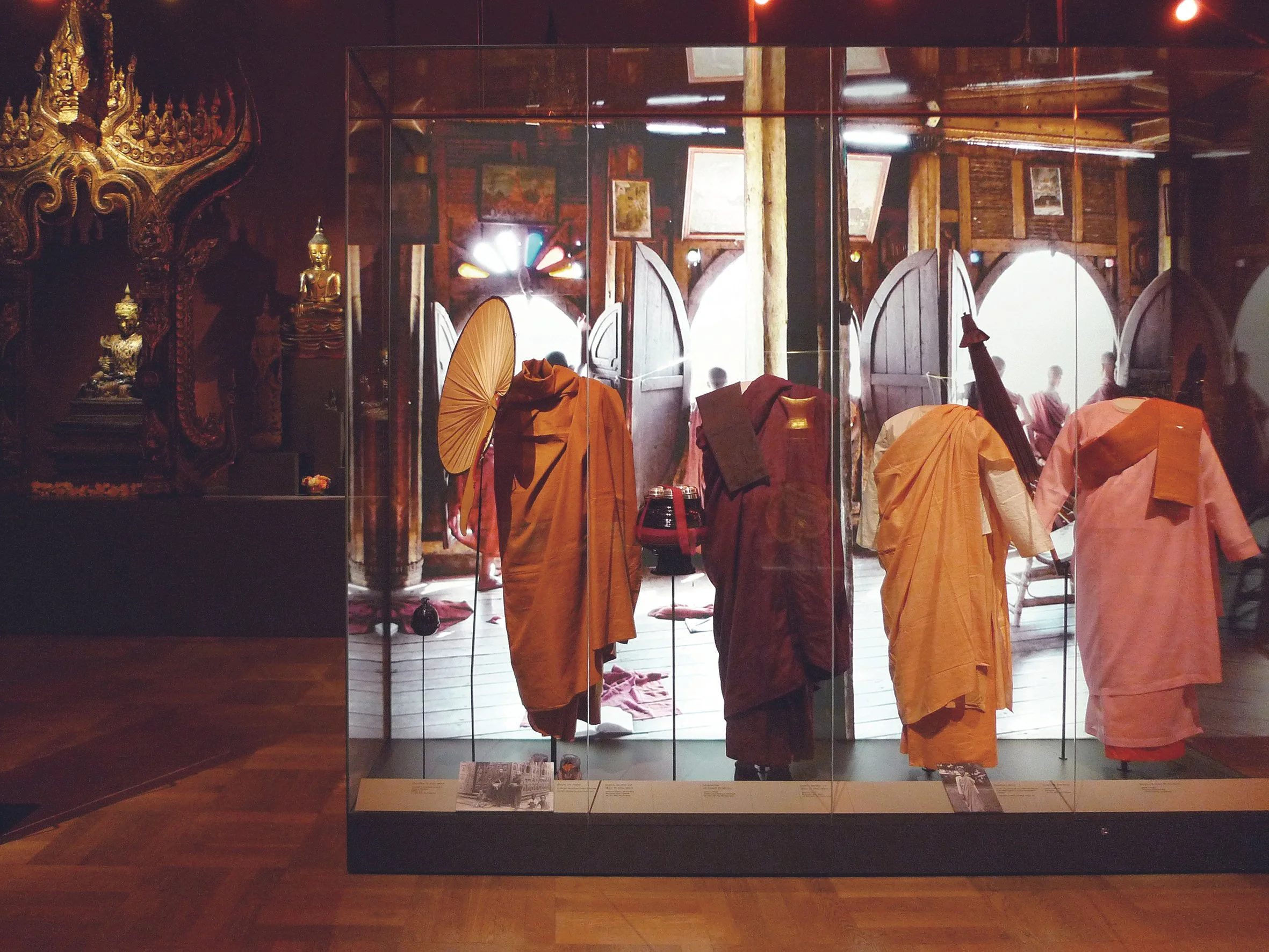 Buddhistische Gewänder und Schirme in einem Museum, hinter einer Glasvitrine.
