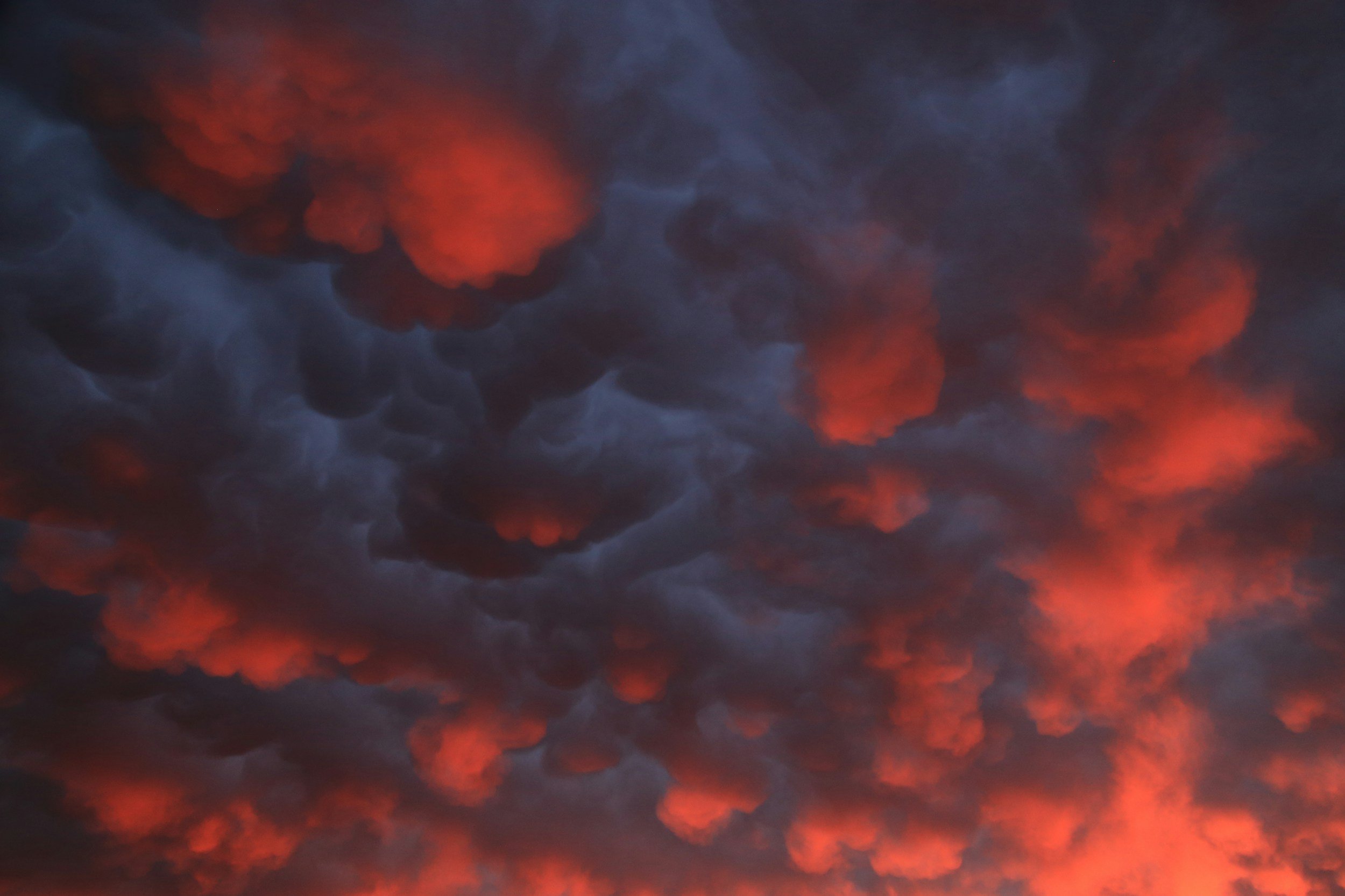 Aerial view of dark smoke clouds with bright orange flames or glow within, indicating a fire or wildfire.