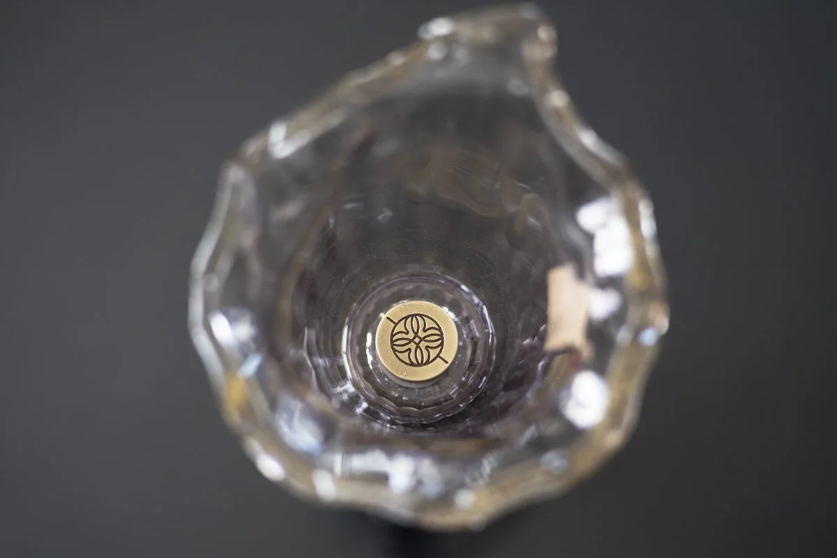 Looking down into an empty crystal glass with a gold sticker at the bottom featuring a black logo.