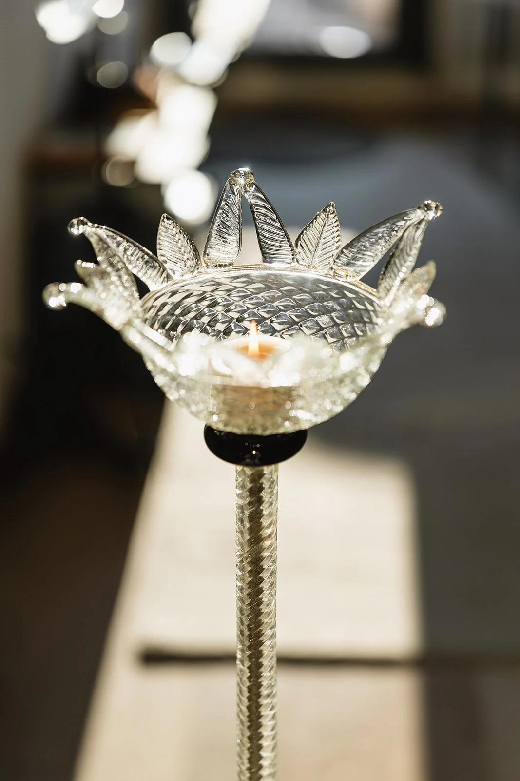 A decorative glass candle holder shaped like a flower with intricate petal details, holding a lit candle inside.