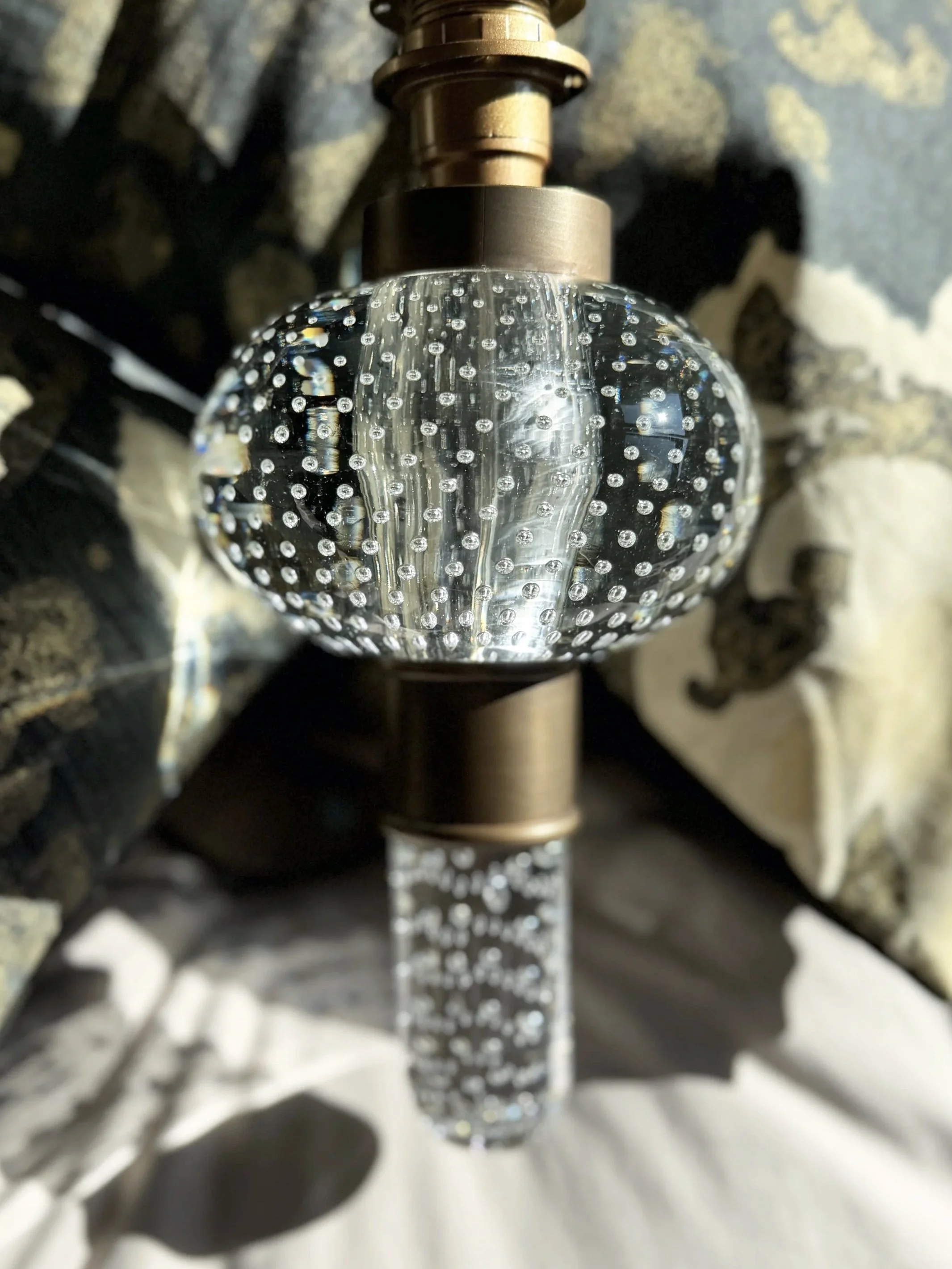 Close-up of a spinning disco ball with small reflective mirrored tiles, mounted on a metallic stand, with patterned shadows cast on a surface.