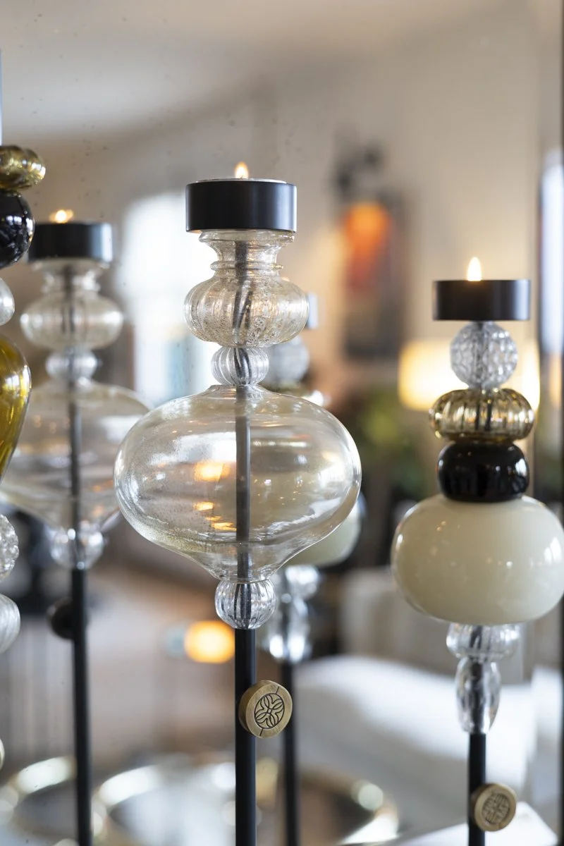 Close-up of decorative glass candle holders with black candles on top, arranged on black metal stands, in a softly lit interior.