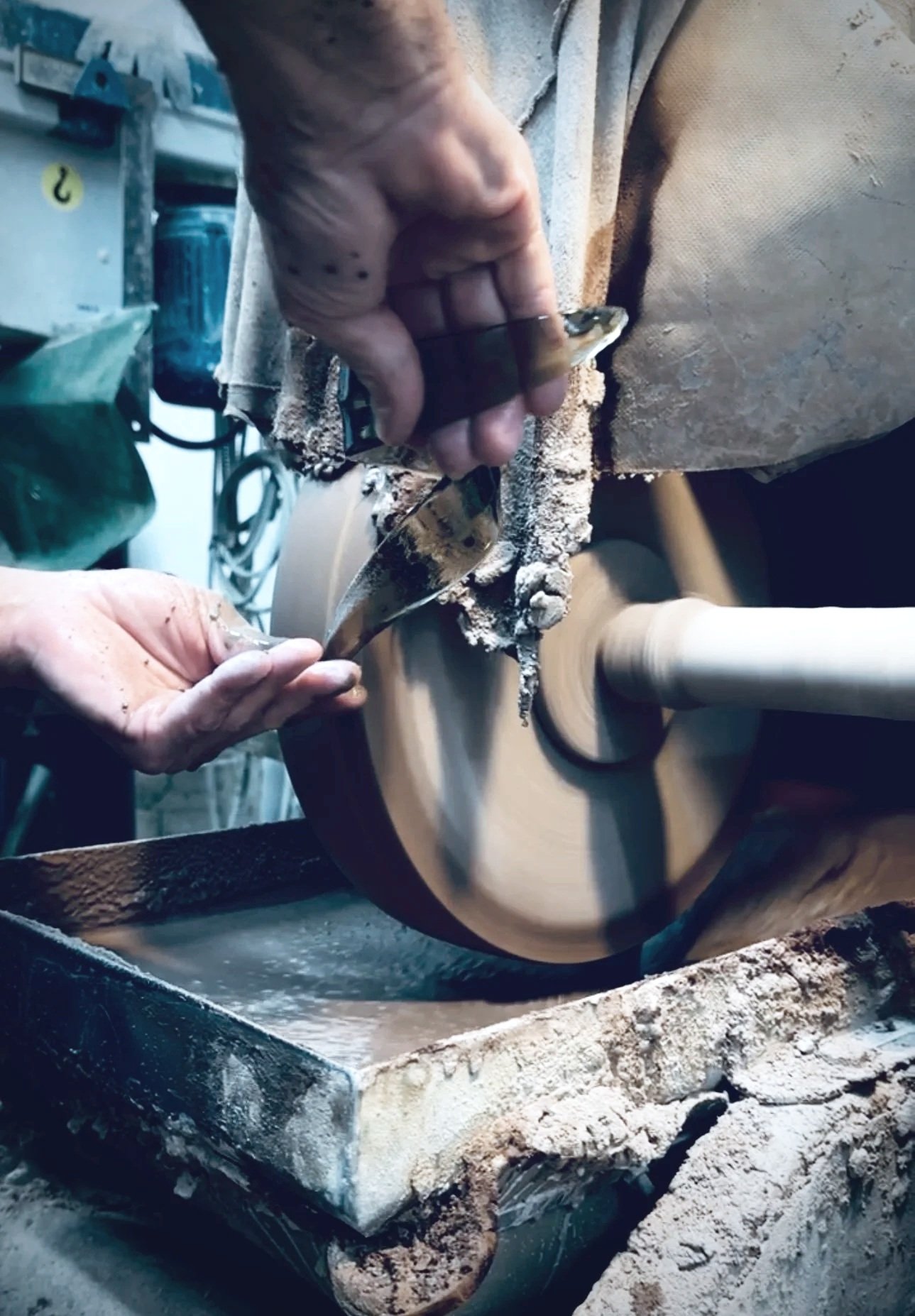 A person using a wood lathe to turn a piece of wood, with sawdust flying and tools nearby.