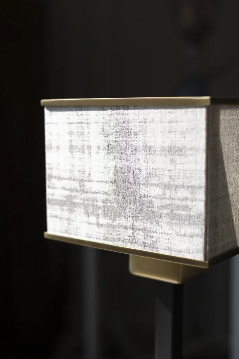 Close-up of a wall-mounted light fixture with a fabric shade and gold accents, with a dark background.