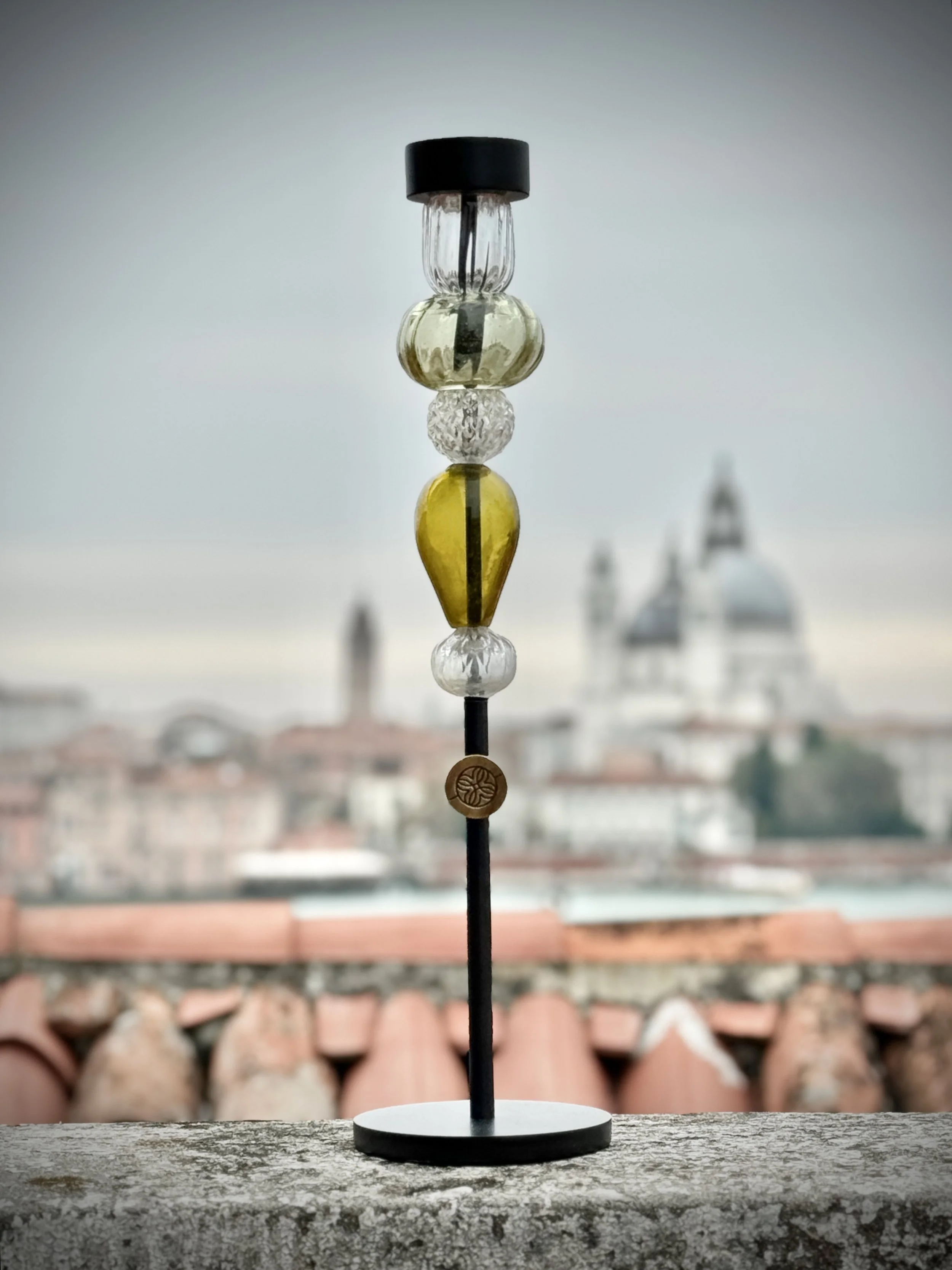 Decorative beaded ornament on a black stand with a background of blurred red roof tiles and gray sky.