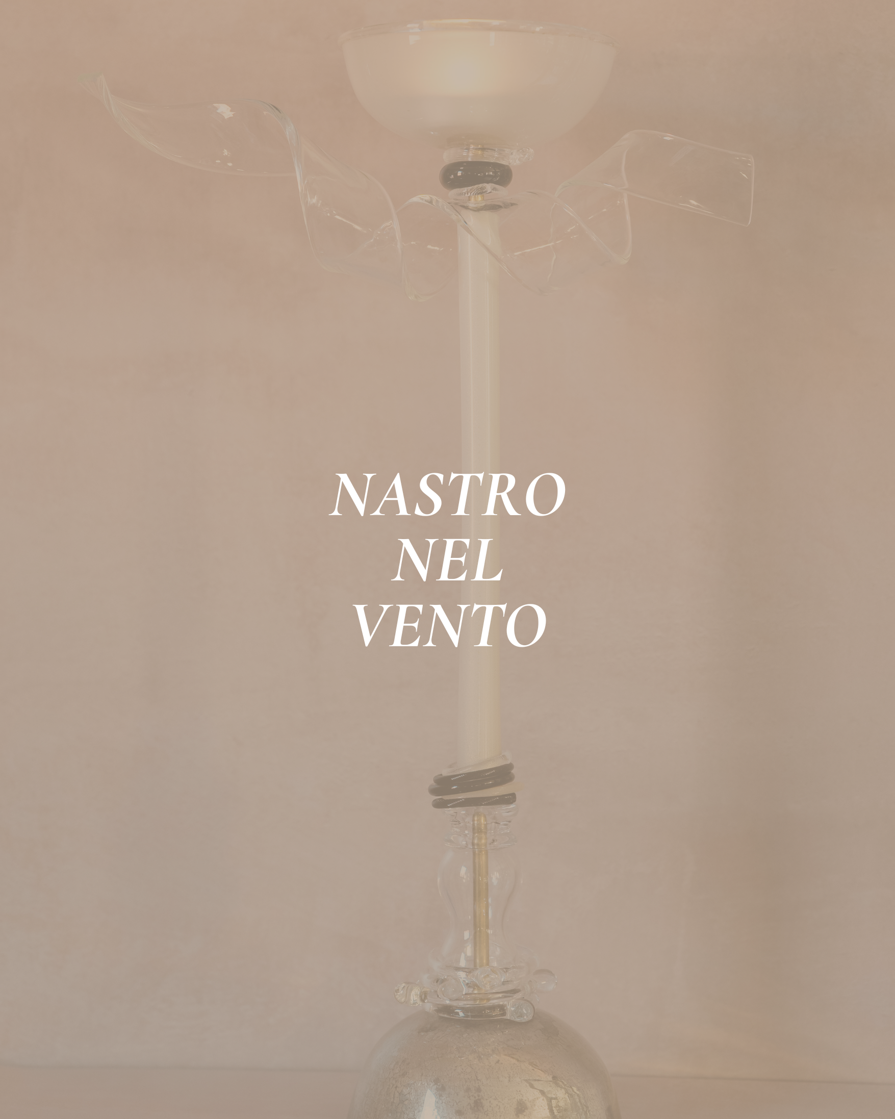 Upside down image of a glass with a long, thin stem, possibly a wine glass, with a decorative black band around the neck, and a large rounded bowl at the top. The background is a plain, neutral color. The text "NASTRO NEI VENTO" is overlaid in white, capitalized serif font.