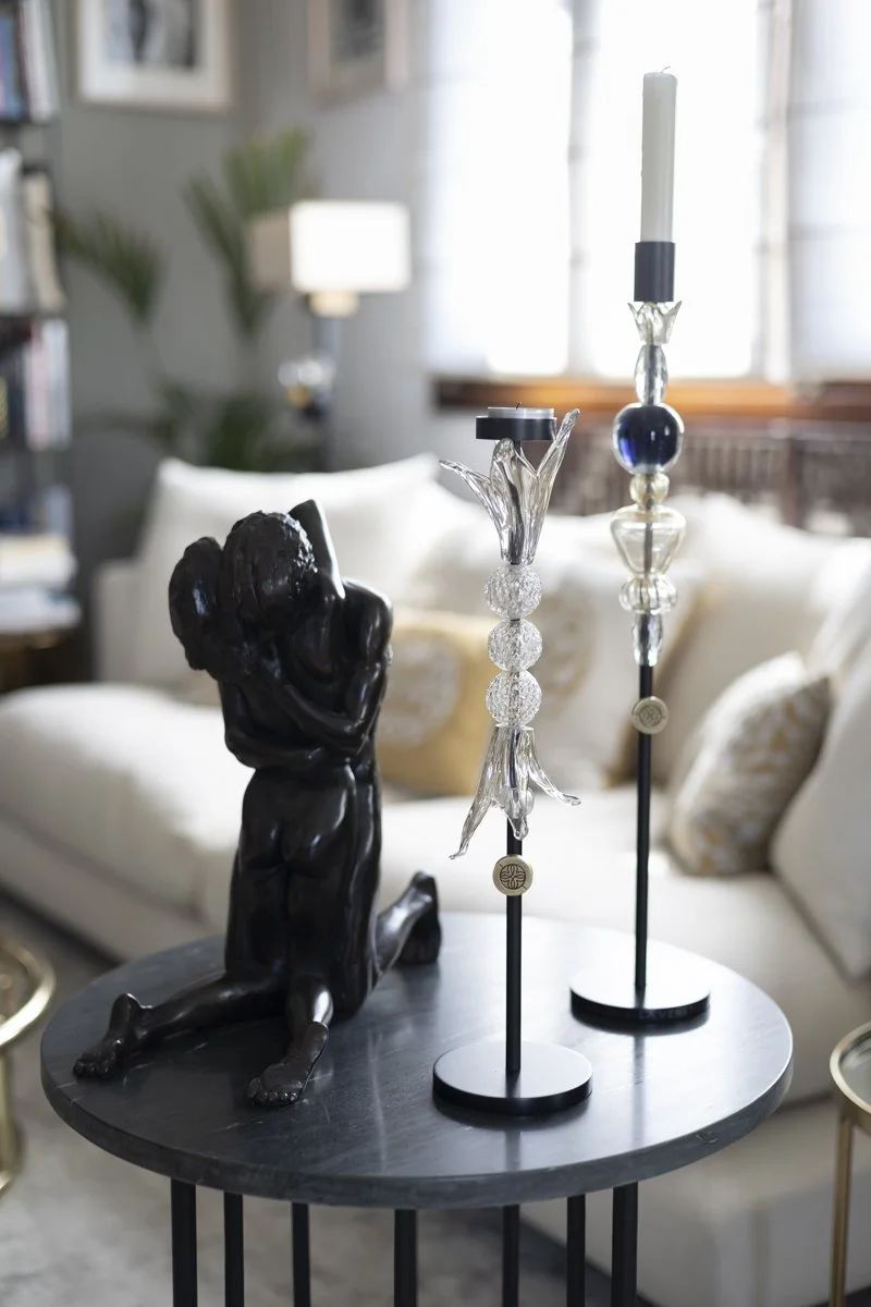 A black sculpture of a dog with a human head holding a smaller figure, alongside two modern candlesticks with white candles, on a round black table in a living room.