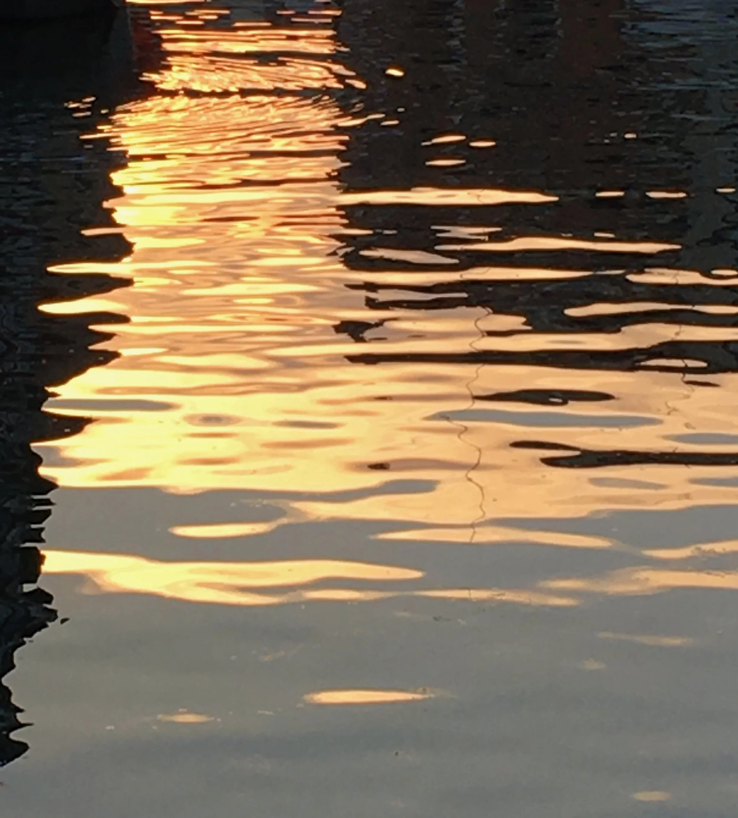 Reflection of orange and yellow sunset on calm water surface with ripples.