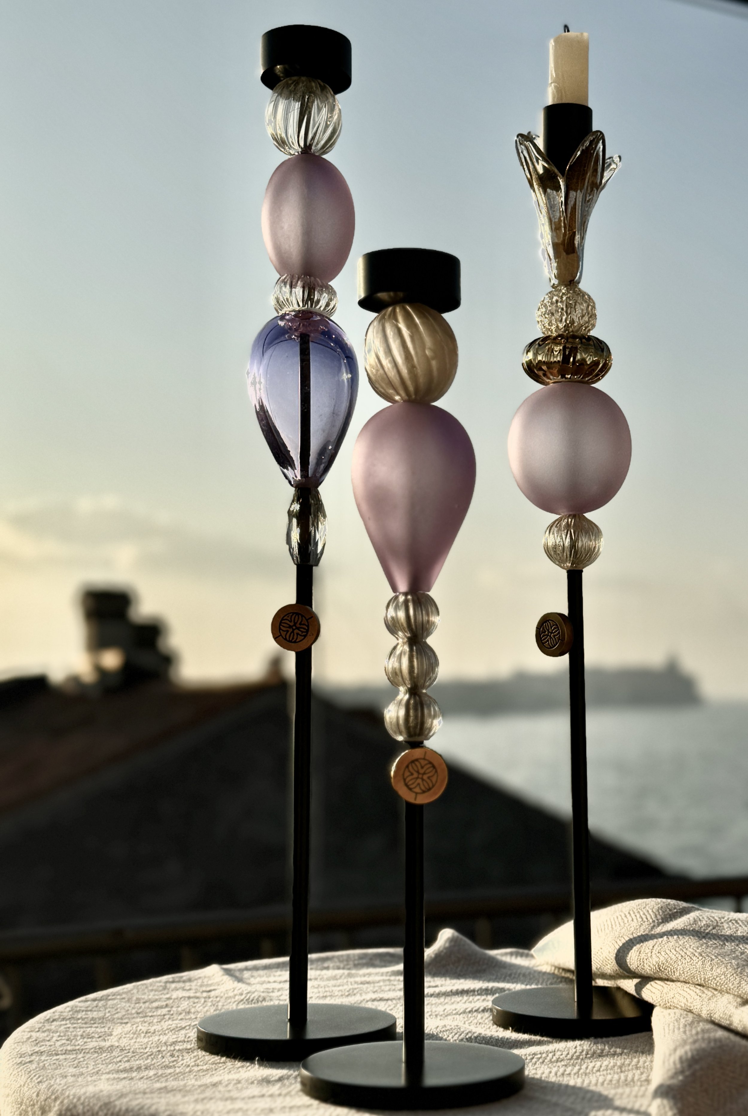 Three decorative glass beaded objects on black stands with a white fabric surface and a sunset sky in the background.