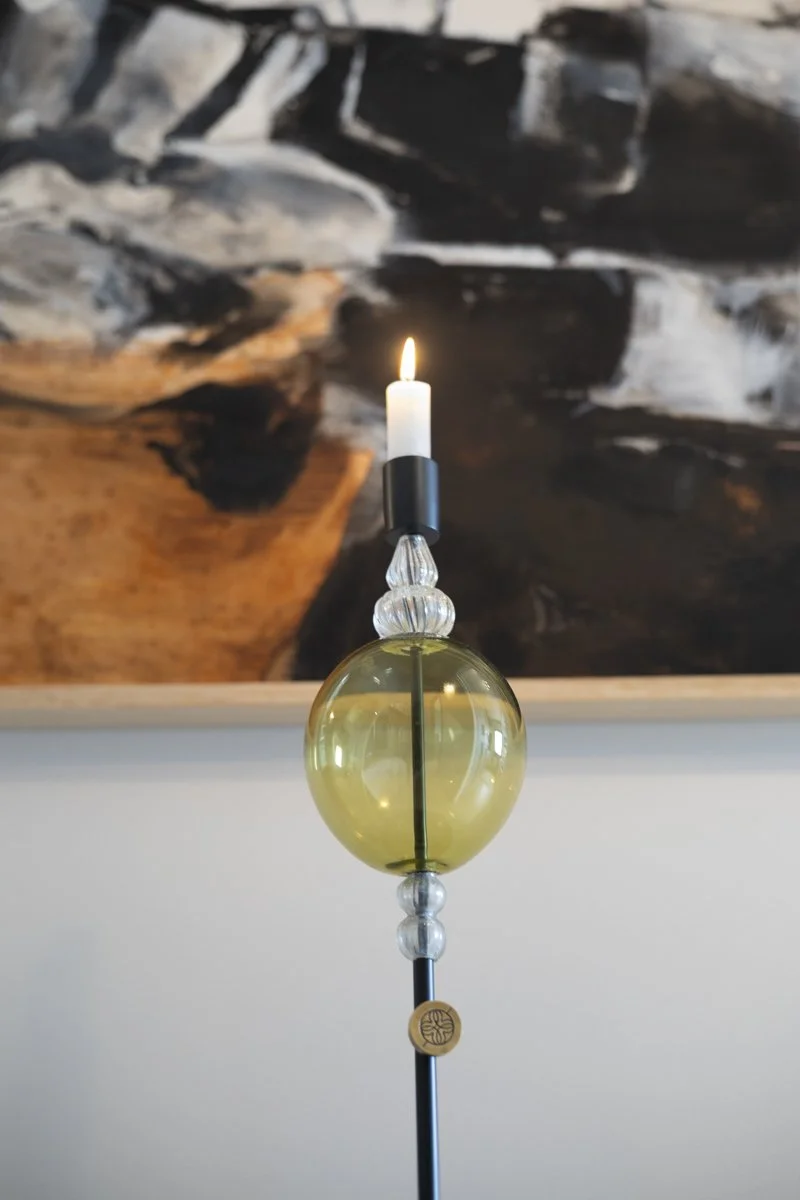 A decorative lamp with a candle-shaped bulb on top and a large yellow glass sphere in the middle, set against a dark, abstract background.