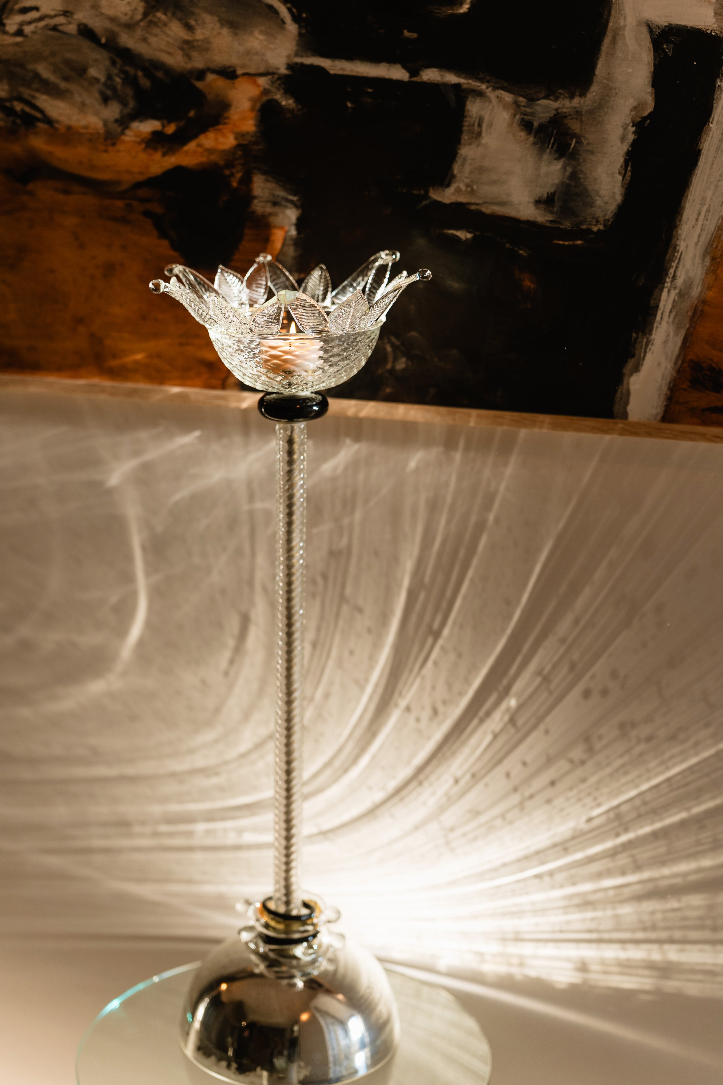Close-up of a crystal table lamp with a decorative shade, reflecting light on a mirrored surface with a dramatic, dark background.