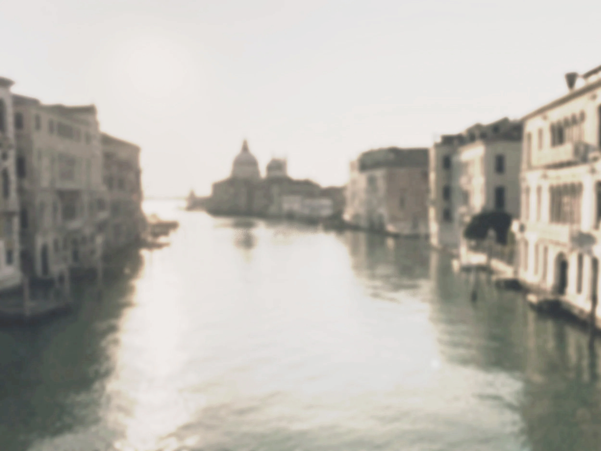 Blurry photo of a cityscape with water and buildings, possibly a canal in Venice.