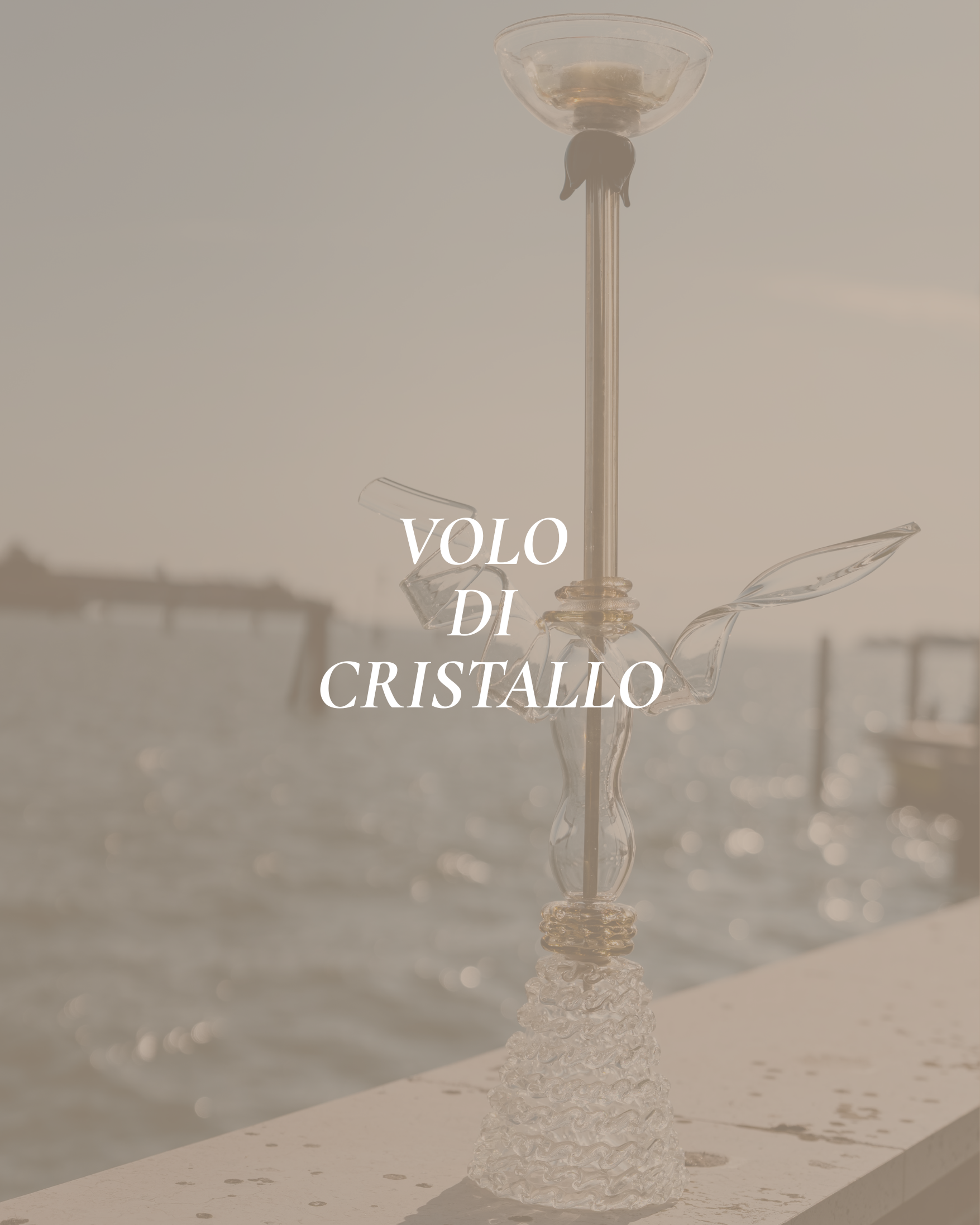 Glass sculpture or decorative piece with a tall, slender, textured stem, a round base, and a rounded bowl or dish at the top, placed on a light-colored surface with a plain background and the partially visible text 'VOLO DI CRISTALLO' in the foreground.