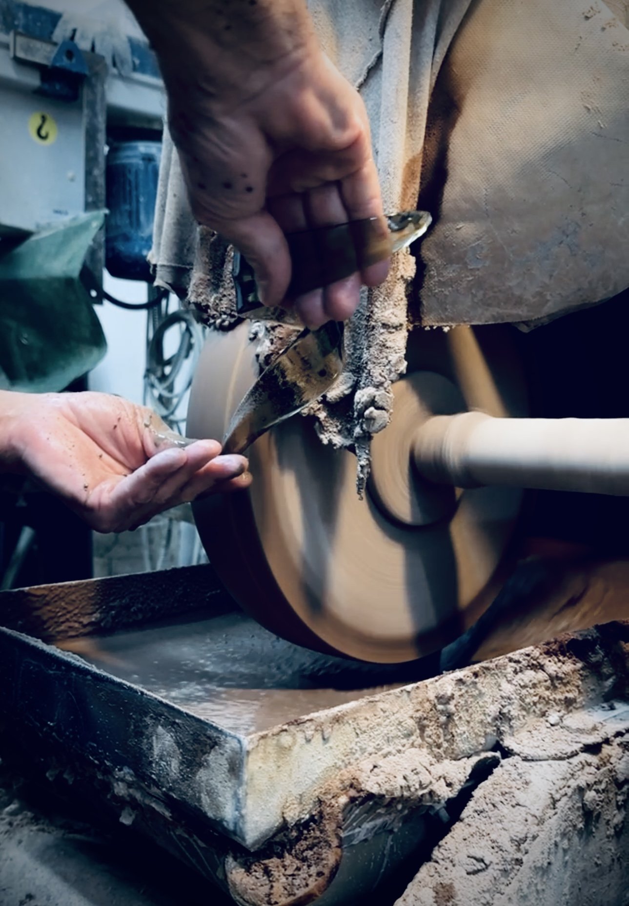 A person is sanding a wooden bowl on a spinning lathe, using a small file, with woodworking tools and equipment visible in the background.